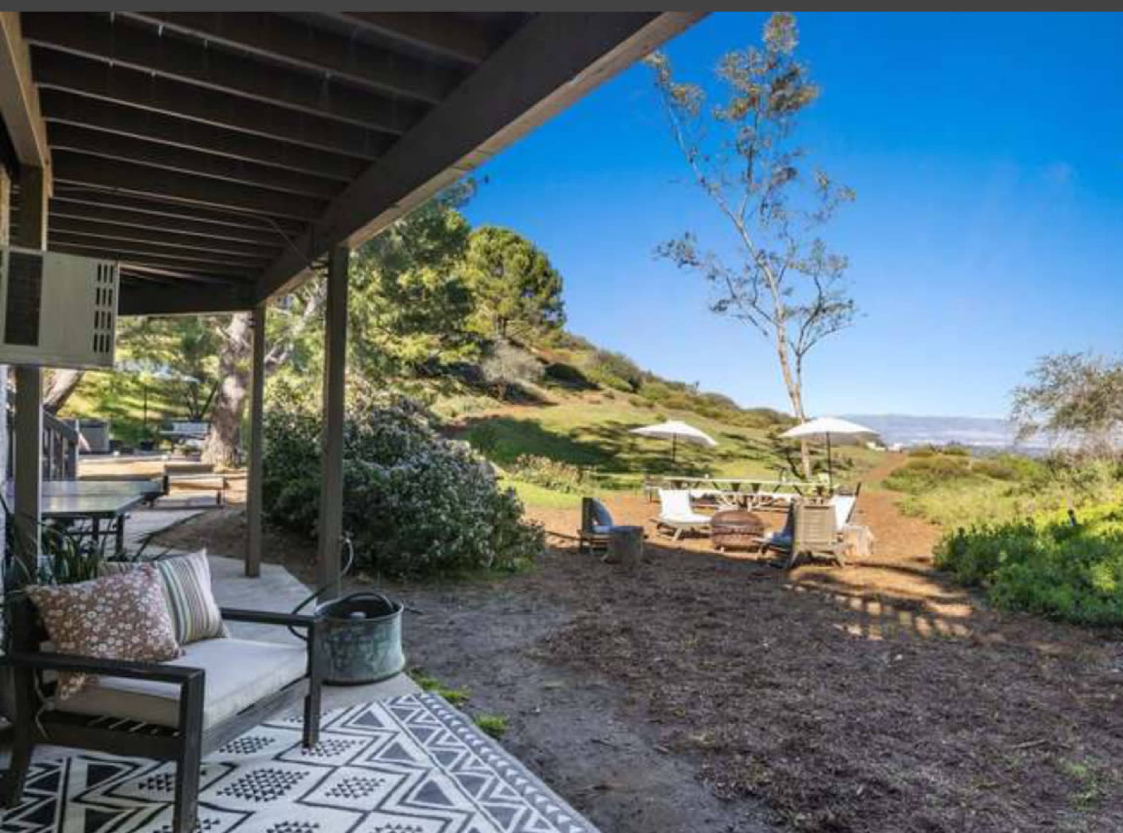 A patio area with seating overlooks a grassy hillside featuring outdoor tables and umbrellas.