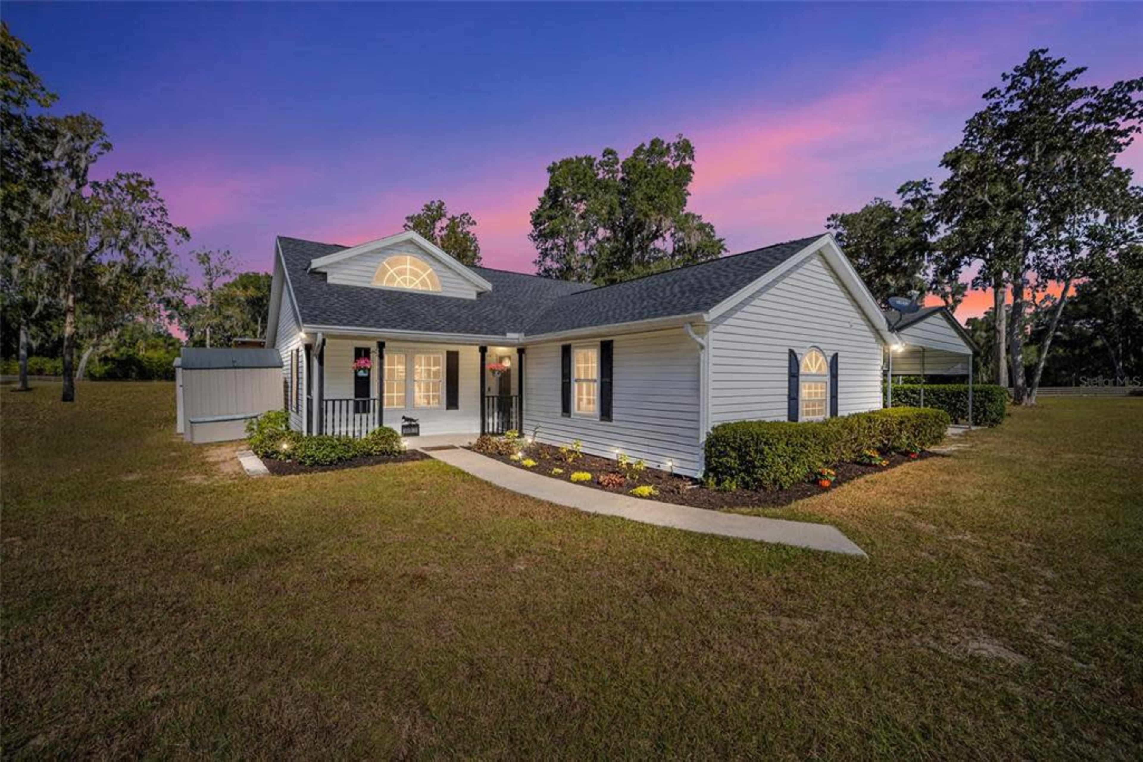 A single-story house with a landscaped front yard, situated under a colorful twilight sky.