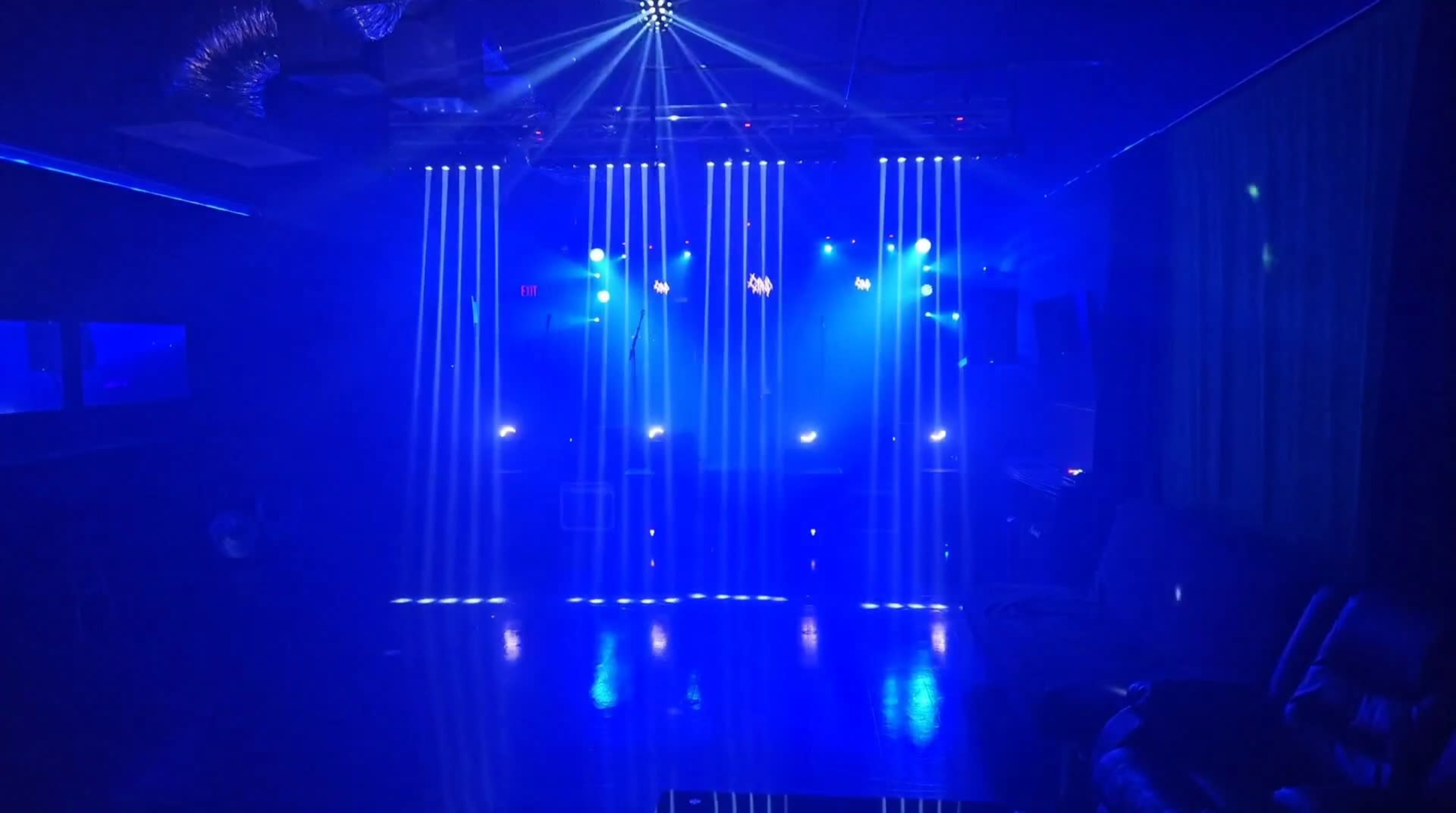 The image shows a dimly lit performance space with blue lighting and vertical beams of light creating a dramatic atmosphere.