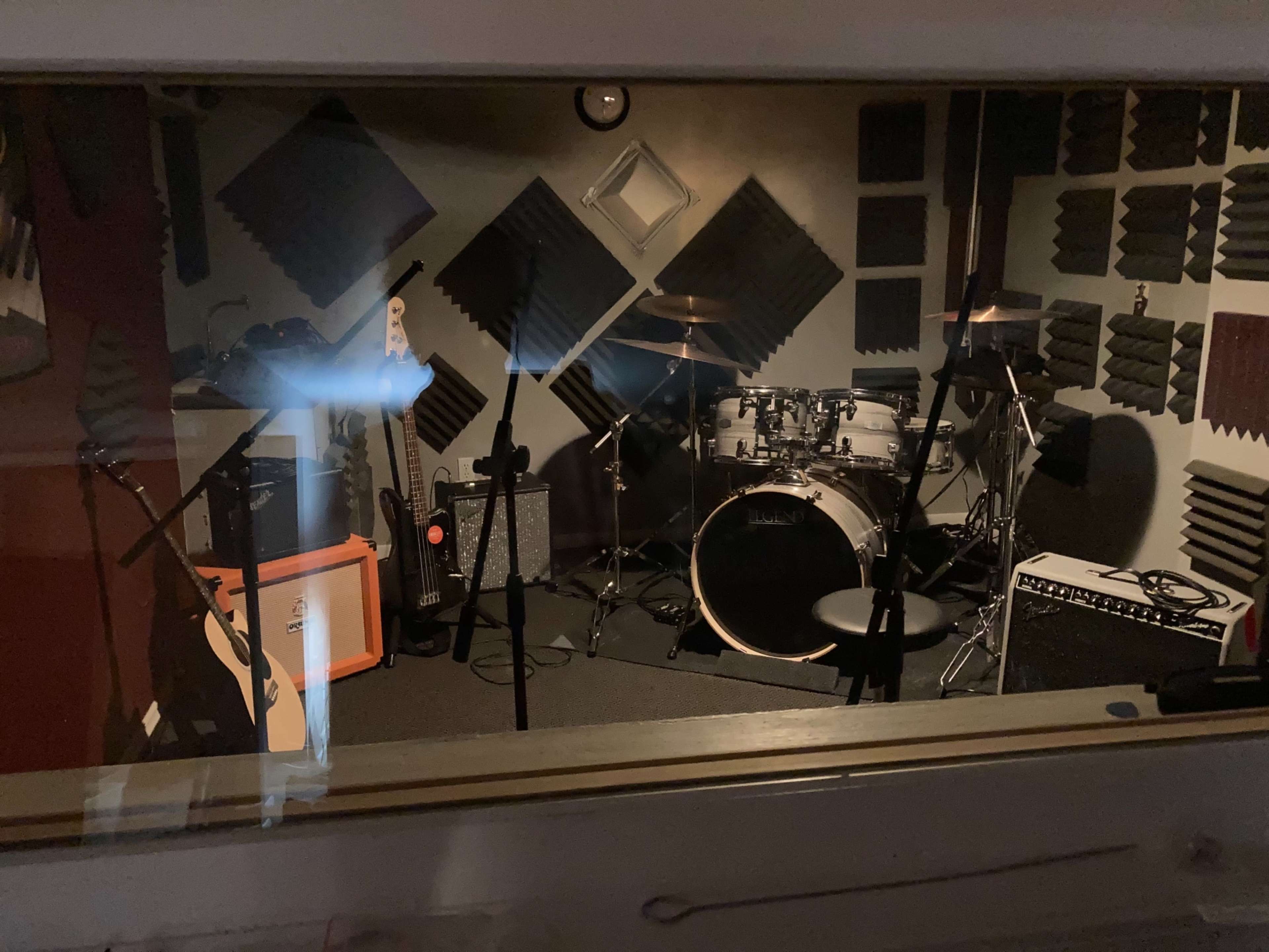 A music practice room containing a drum set, amplifiers, microphones, and various musical instruments surrounded by soundproofing panels.