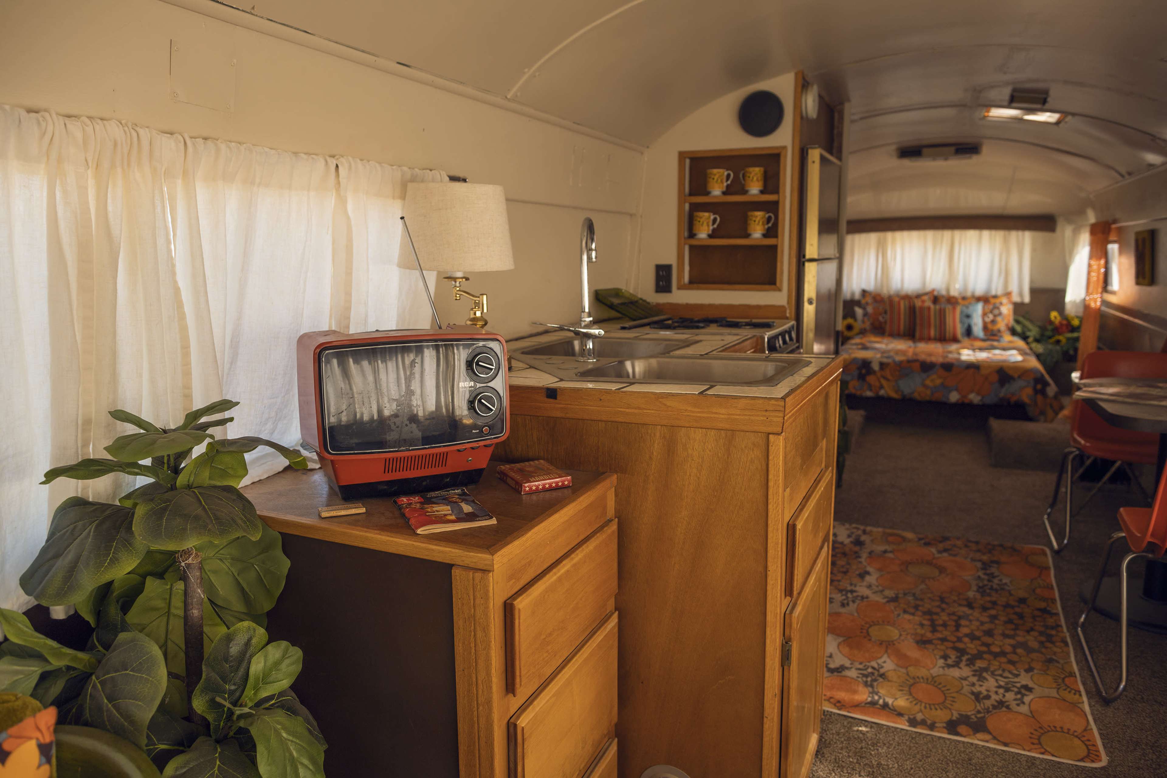 The interior of a retro-style camper features a kitchenette with a small sink, a vintage television, and a seating area adorned with patterned cushions.
