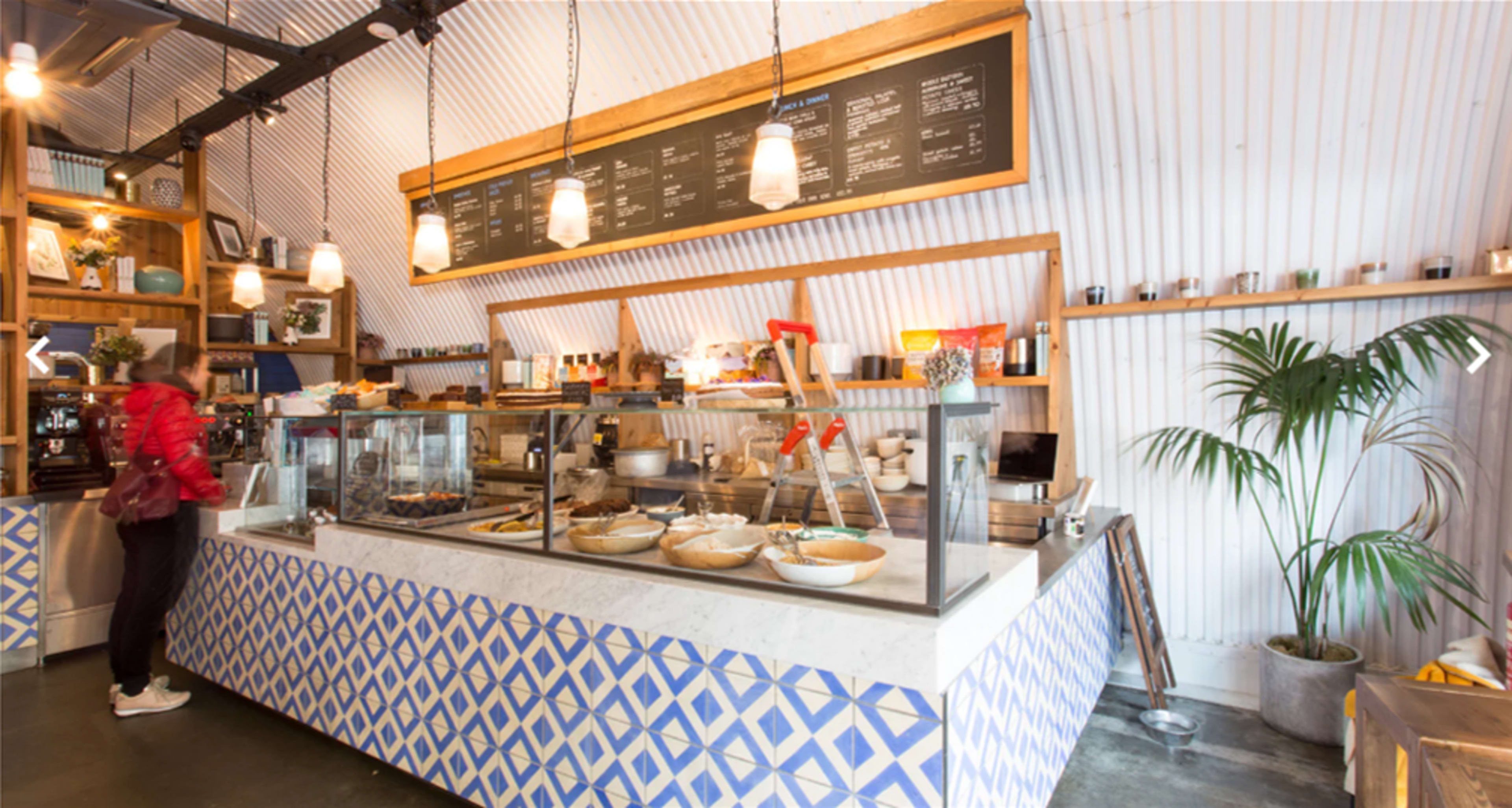 A customer stands at the counter of a cafe with a menu displayed above and a decorative blue and white patterned design on the service area.