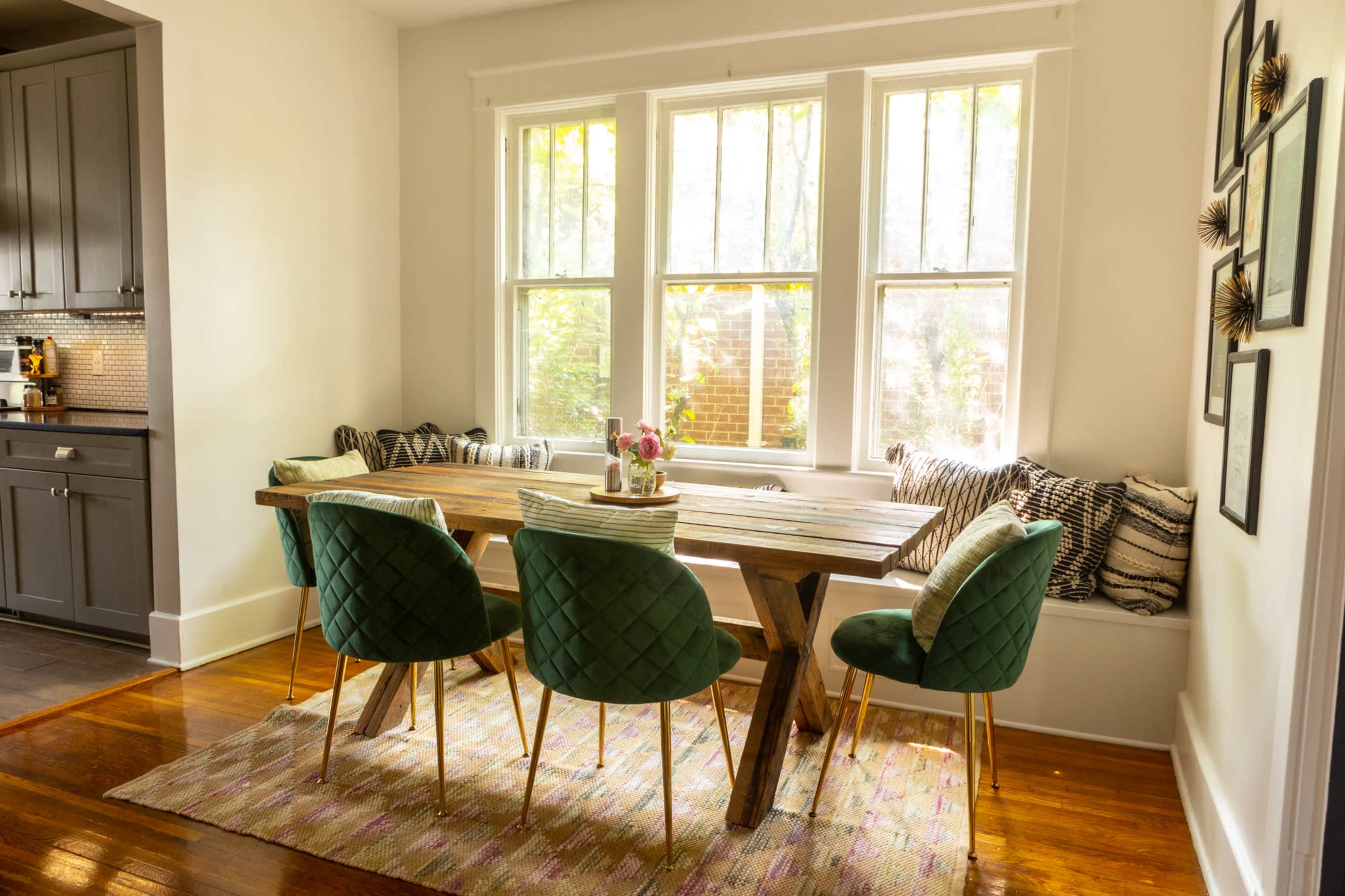 A dining area features a wooden table surrounded by green upholstered chairs and a window seat with decorative pillows.