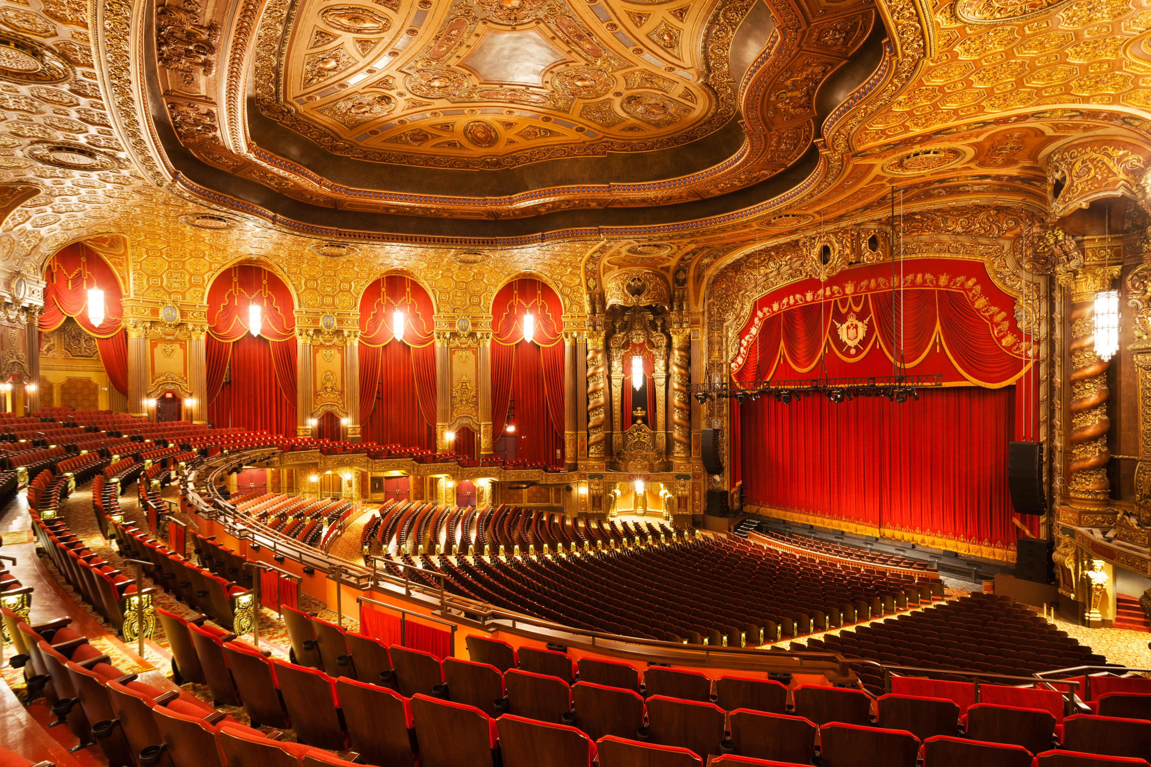 The interior of a grand theater features ornate ceilings, red curtains, and rows of plush seats facing the stage.