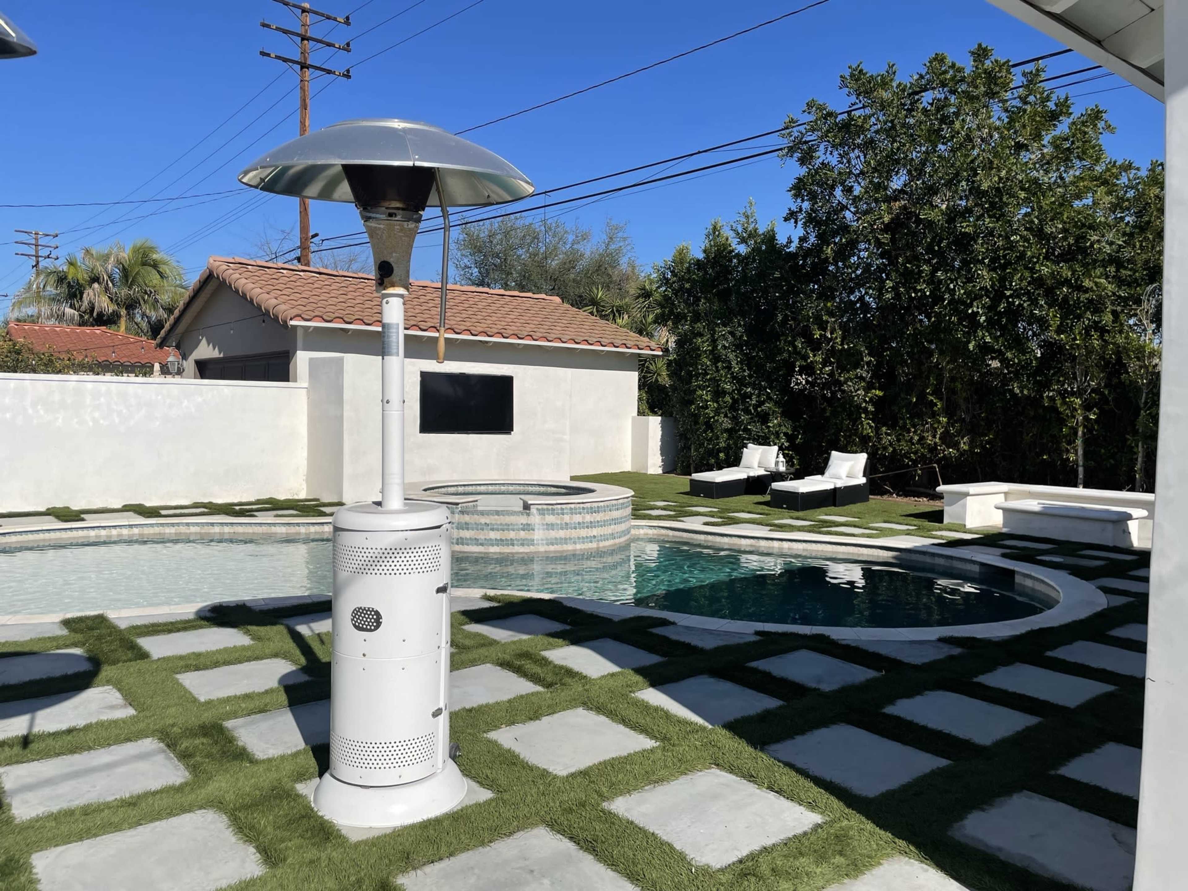 The scene features a backyard with a circular pool, a raised spa, a patio heater, and landscaped areas of grass and stone pavers.