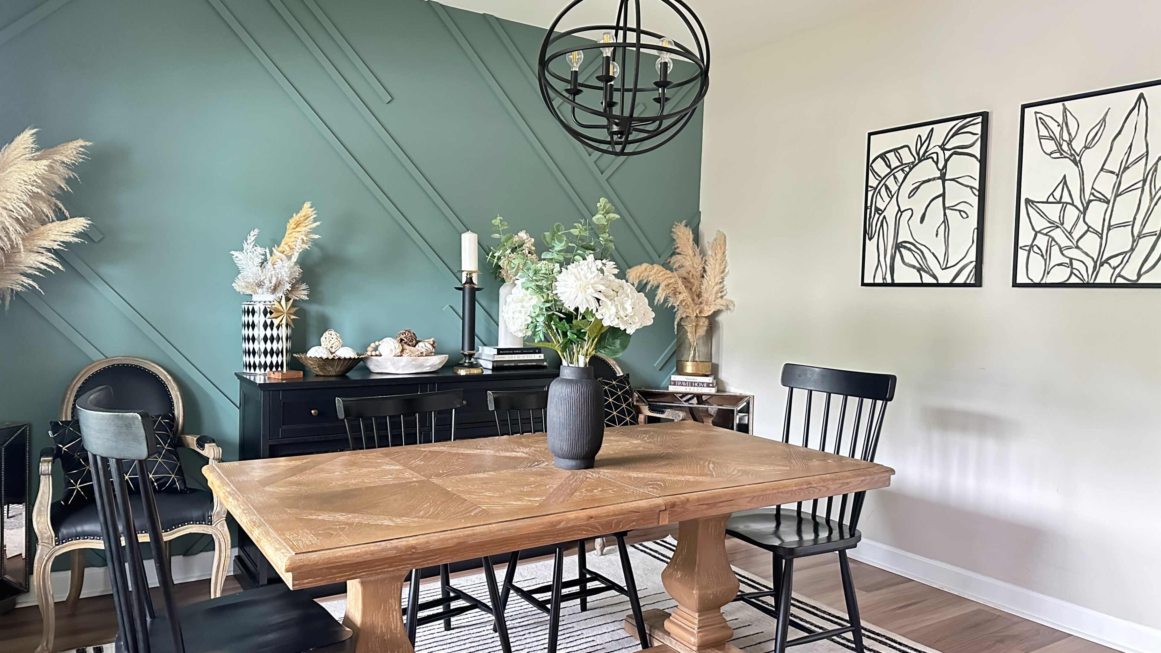 A dining area featuring a wooden table surrounded by black chairs, with a teal accent wall, decorative plants, and framed artwork on the adjacent wall.