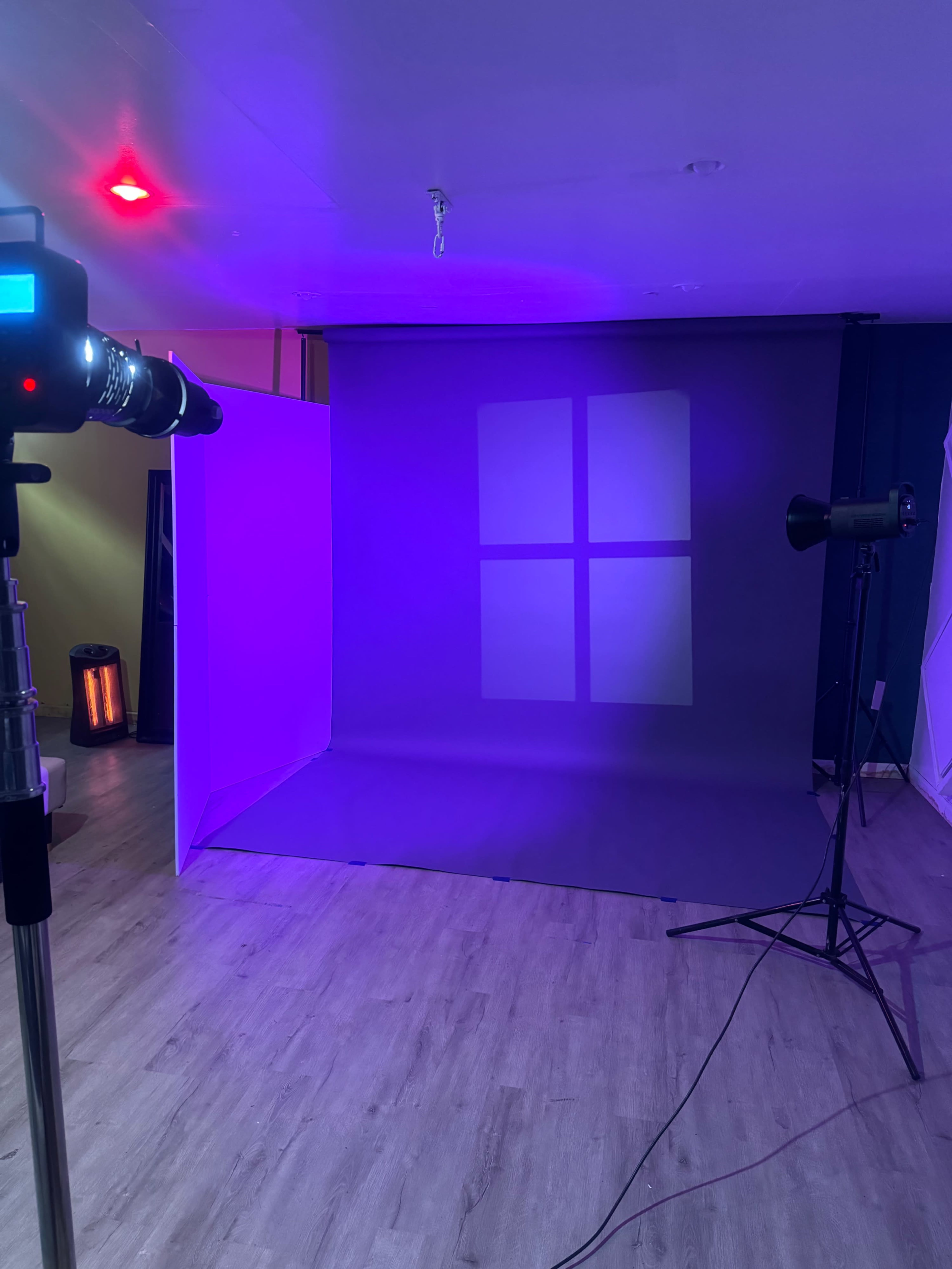 A photography studio setup featuring a backdrop with soft lighting, a camera on a tripod, and a spotlight positioned on the side.