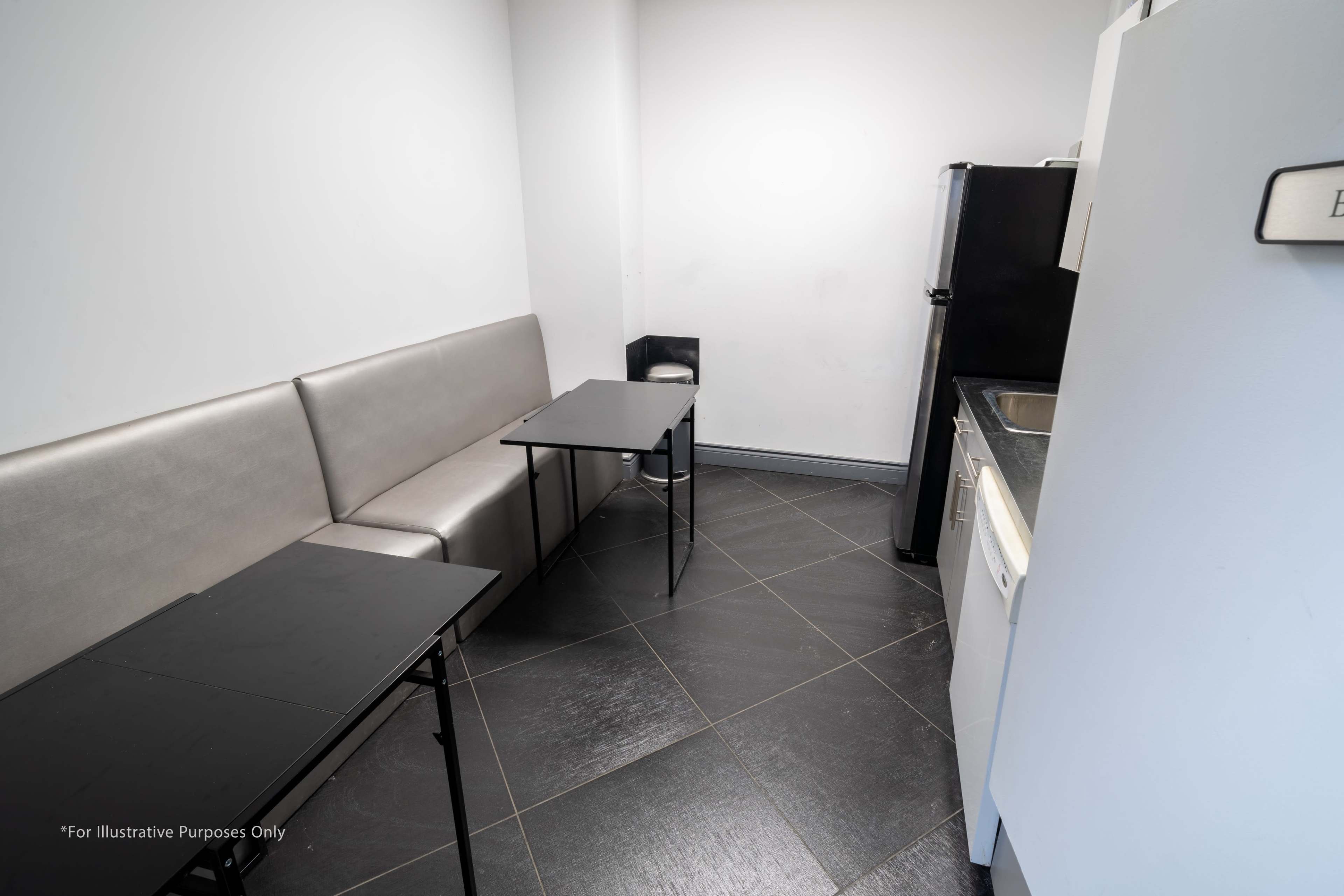 A small kitchen area features a gray seating bench, two black tables, and appliances including a refrigerator and sink.