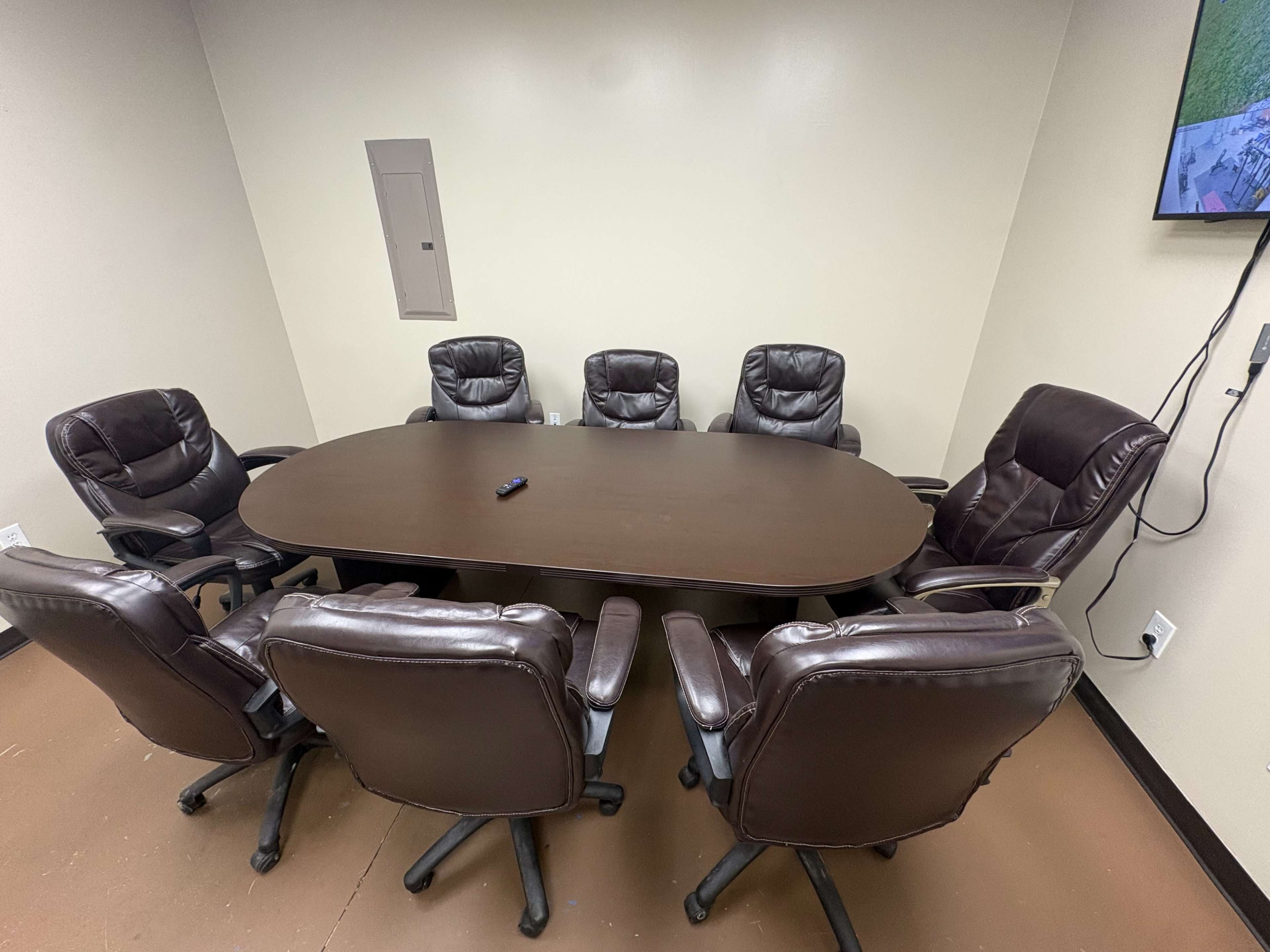 A conference room features an oval table surrounded by six brown leather ergonomic chairs.