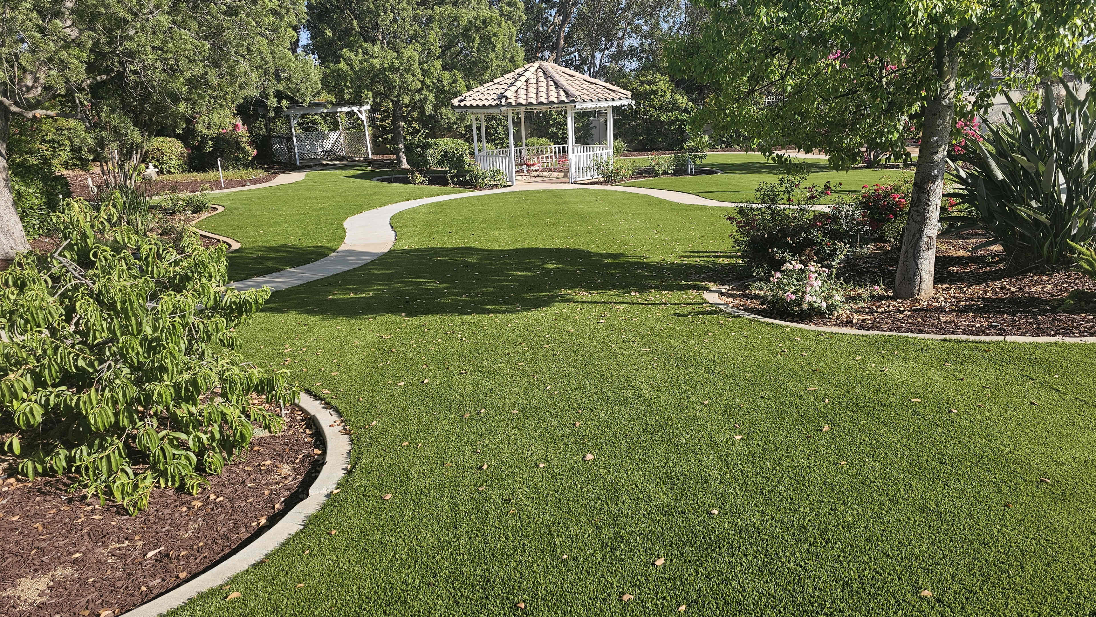 The image shows a landscaped garden with a gazebo surrounded by neatly trimmed grass and flower beds.