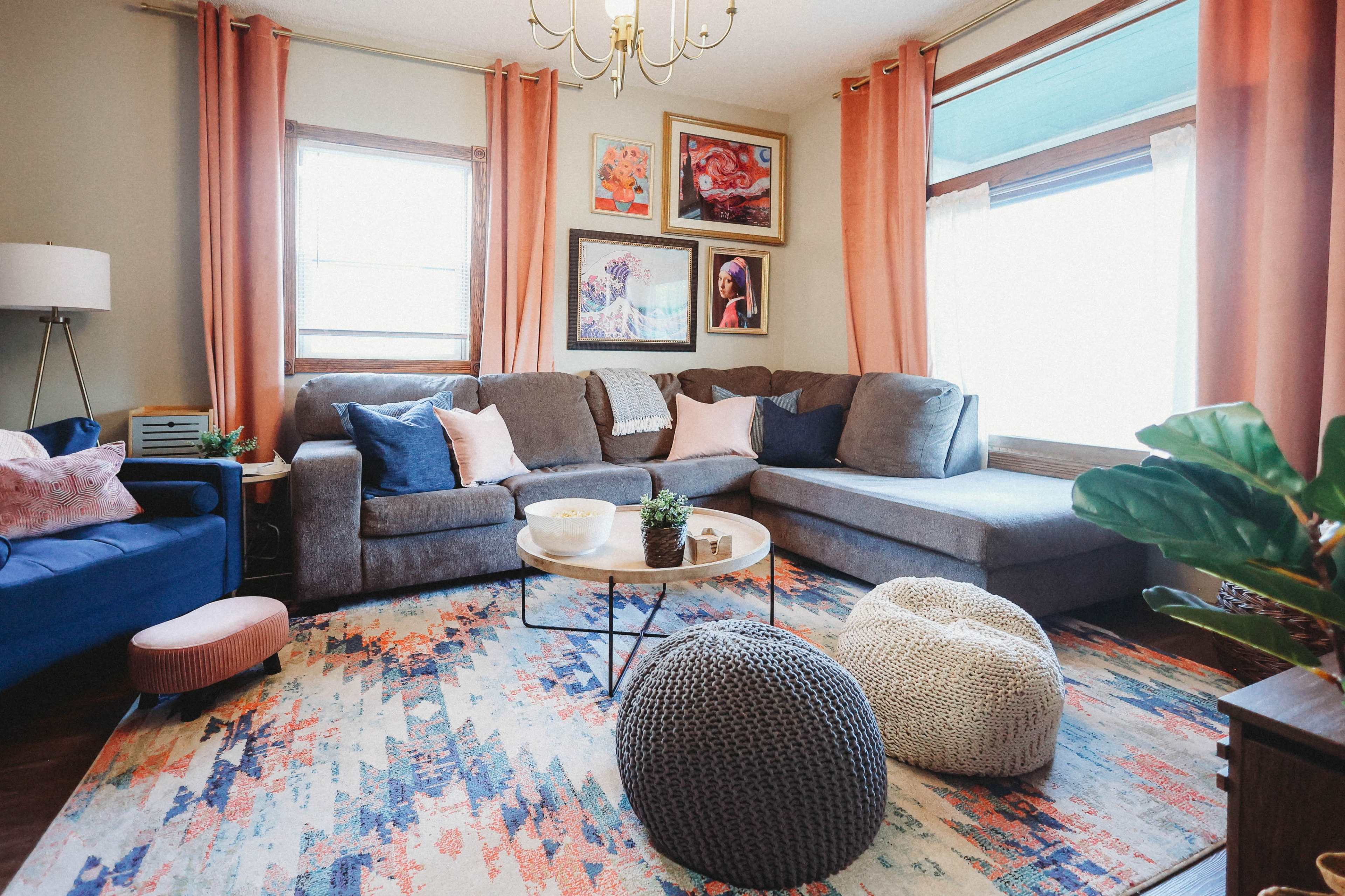 A cozy living room featuring a gray sectional sofa, a round coffee table, colorful artwork on the walls, and various decorative elements like poufs and plants.