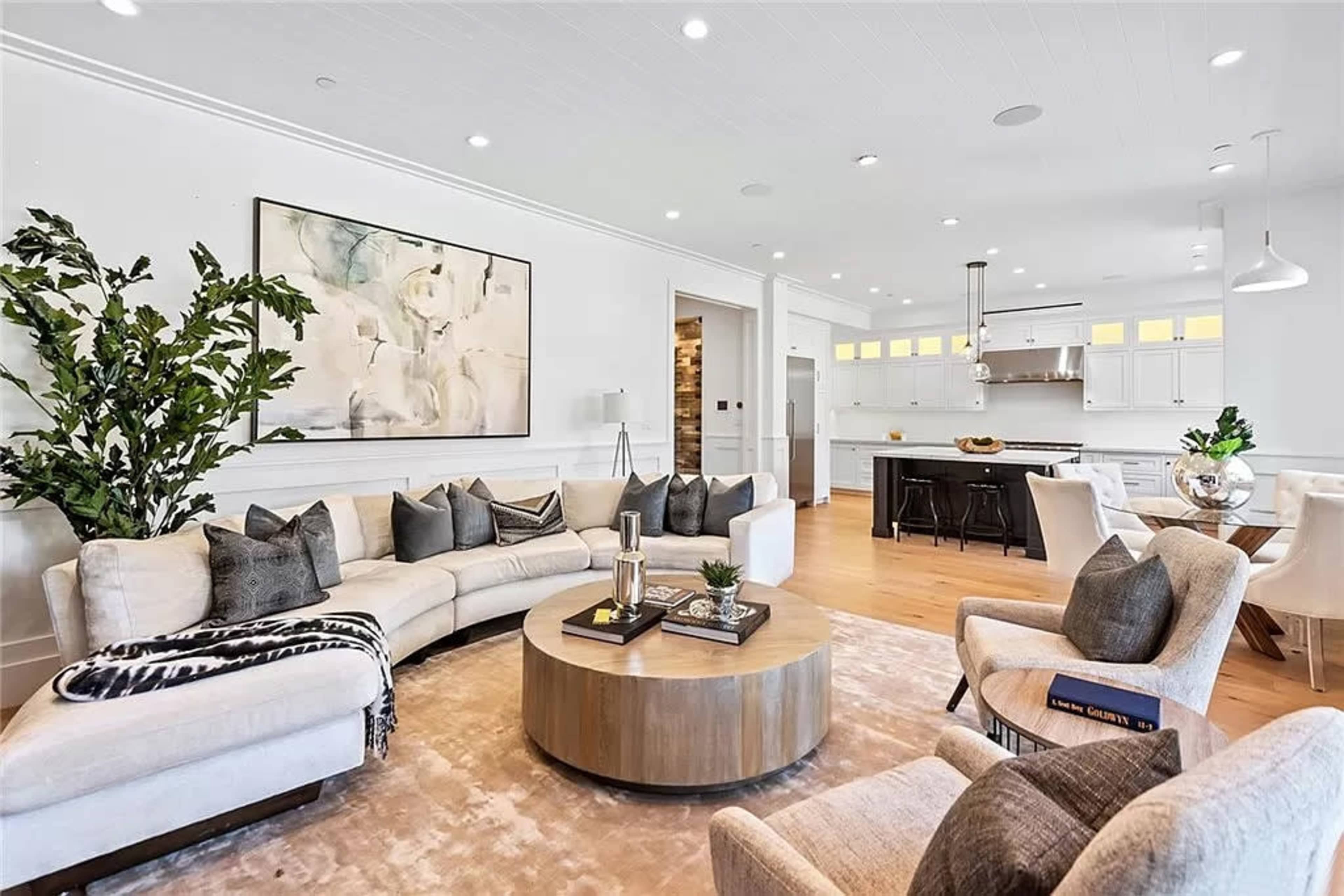 A modern living room with a curved sectional sofa, a round coffee table, and a dining area that includes a kitchen behind it.
