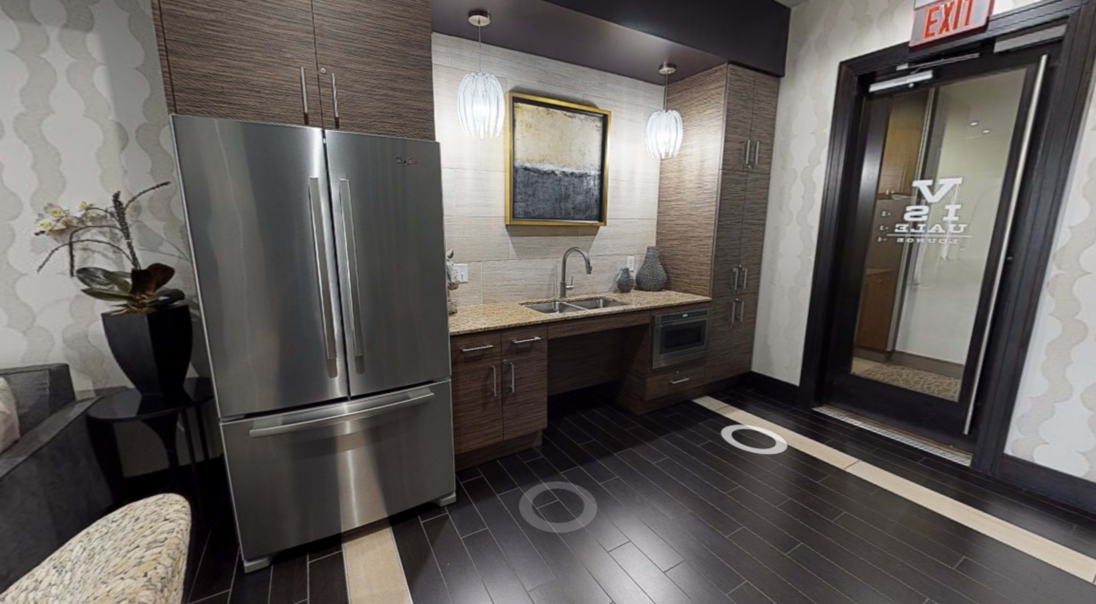 A modern kitchen area with stainless steel appliances, including a refrigerator and a sink, complemented by dark wooden flooring and decorative wall elements.
