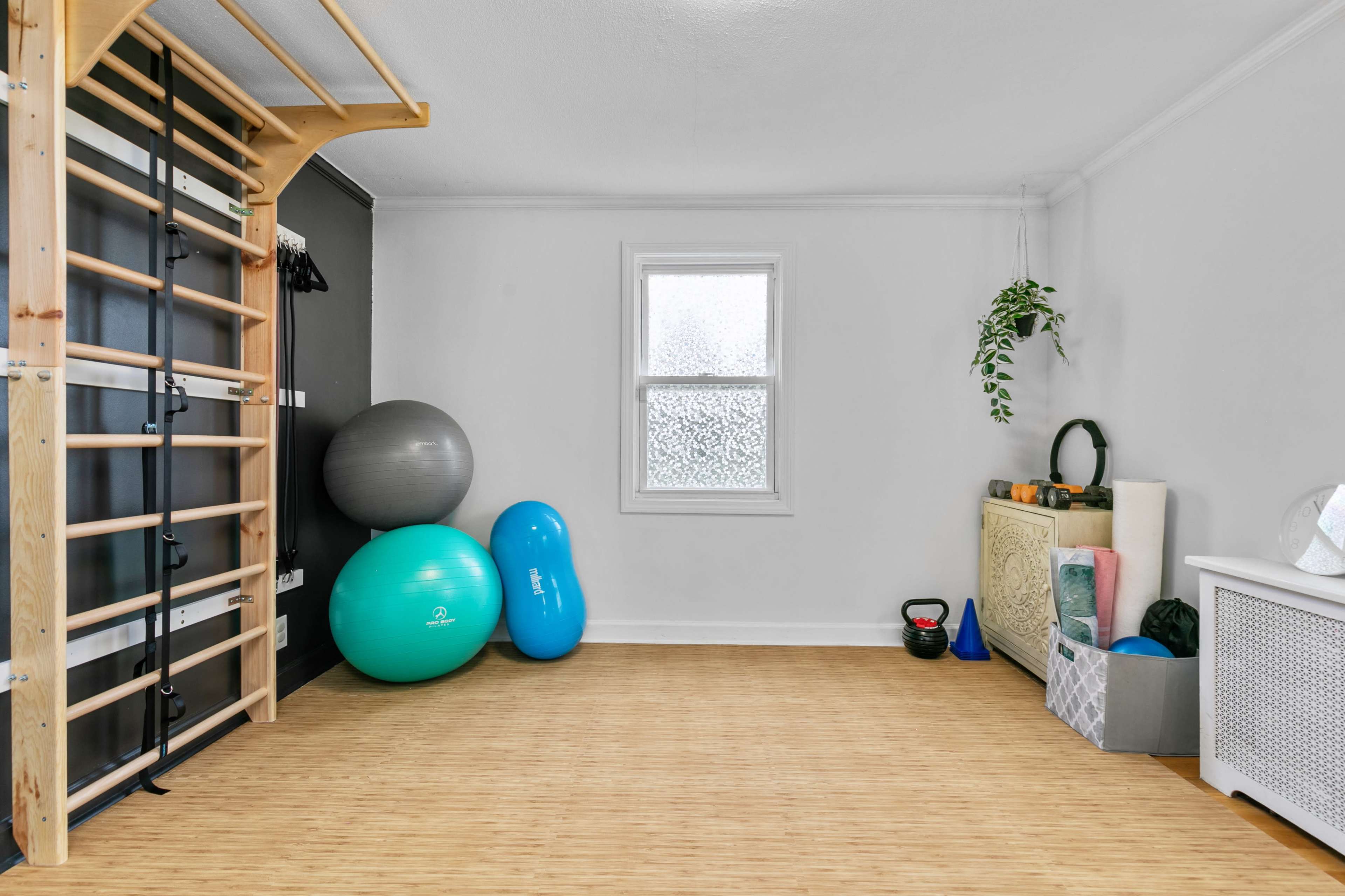 The image shows a fitness area with exercise equipment, including stability balls, a kettlebell, and a wooden wall bar.