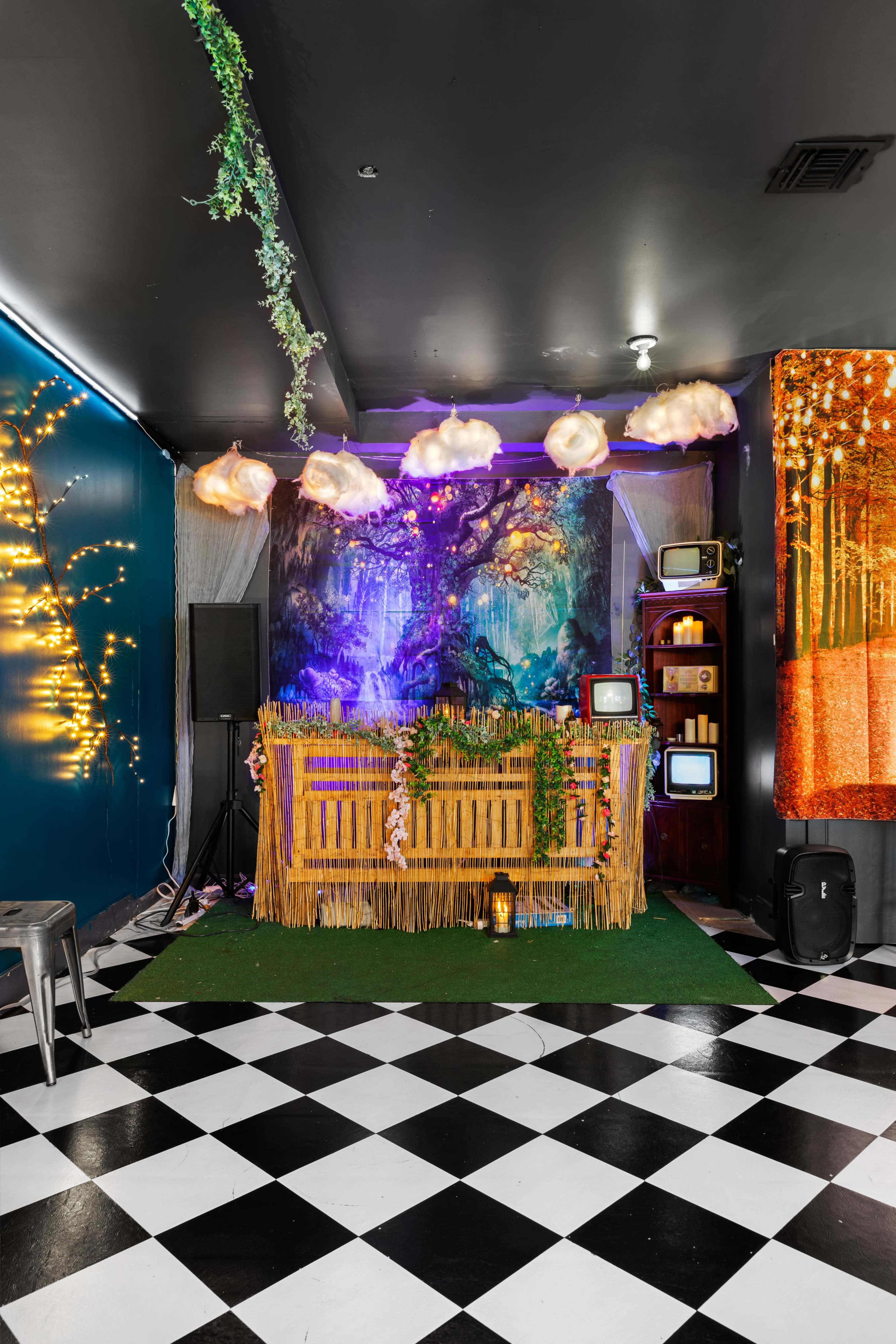 A stylish indoor space featuring a bamboo bar adorned with greenery, colorful lights, and retro televisions against a vibrant mural backdrop.