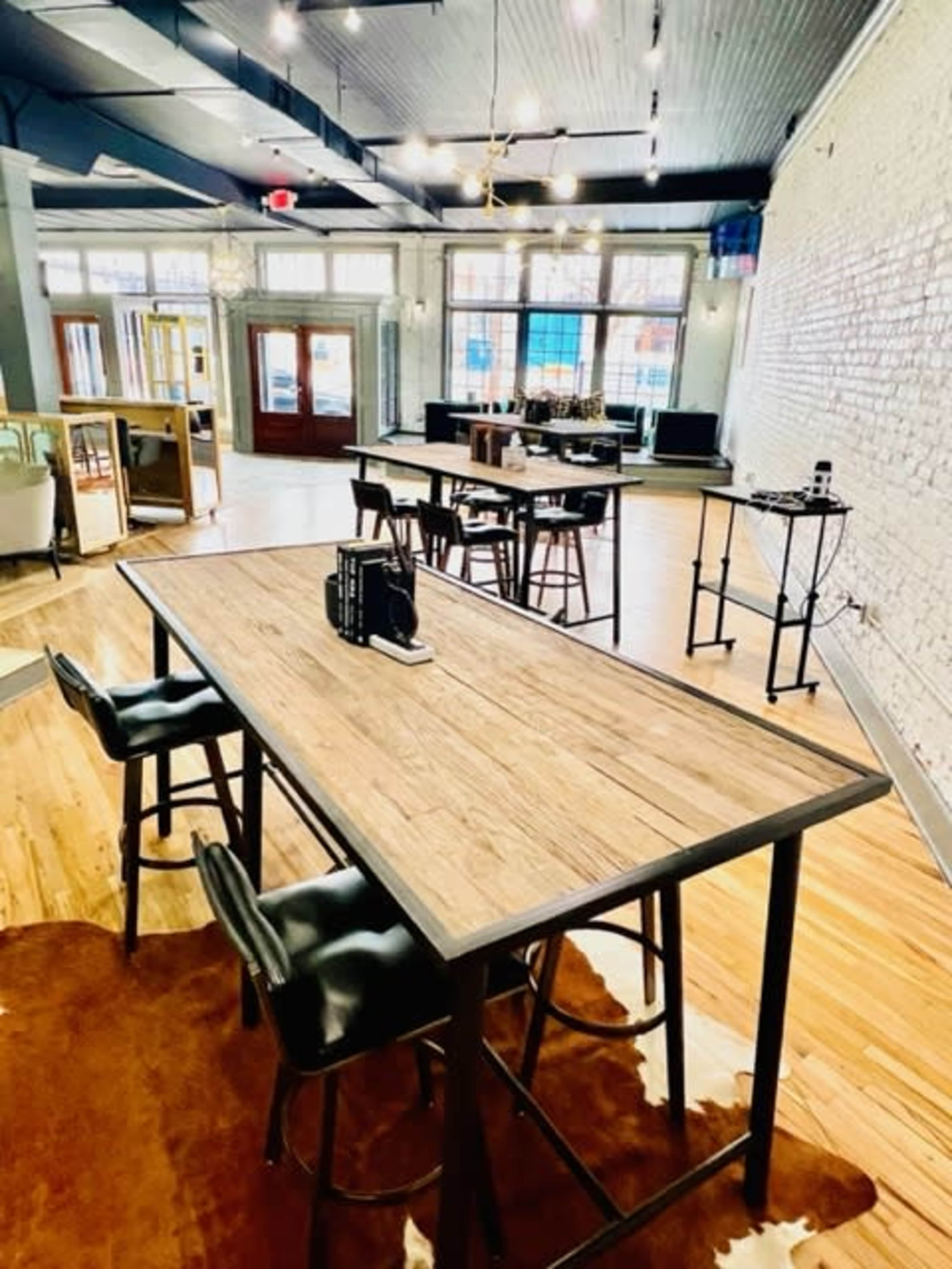 A spacious, modern workspace with several wooden tables and black chairs arranged on a hardwood floor.