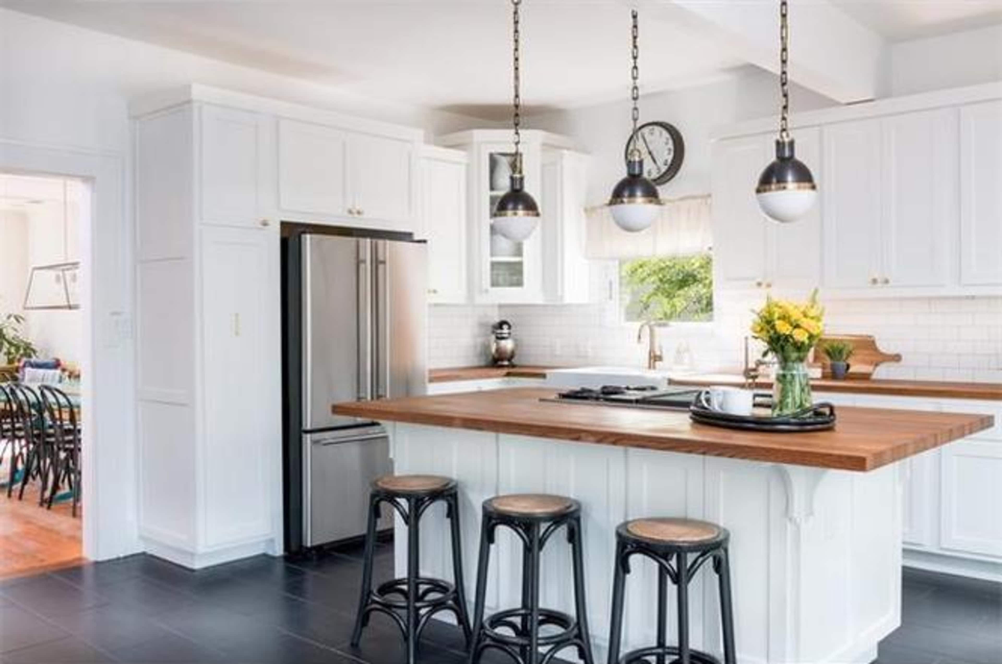 A modern kitchen features white cabinetry, a large wooden island with bar stools, and pendant lighting.