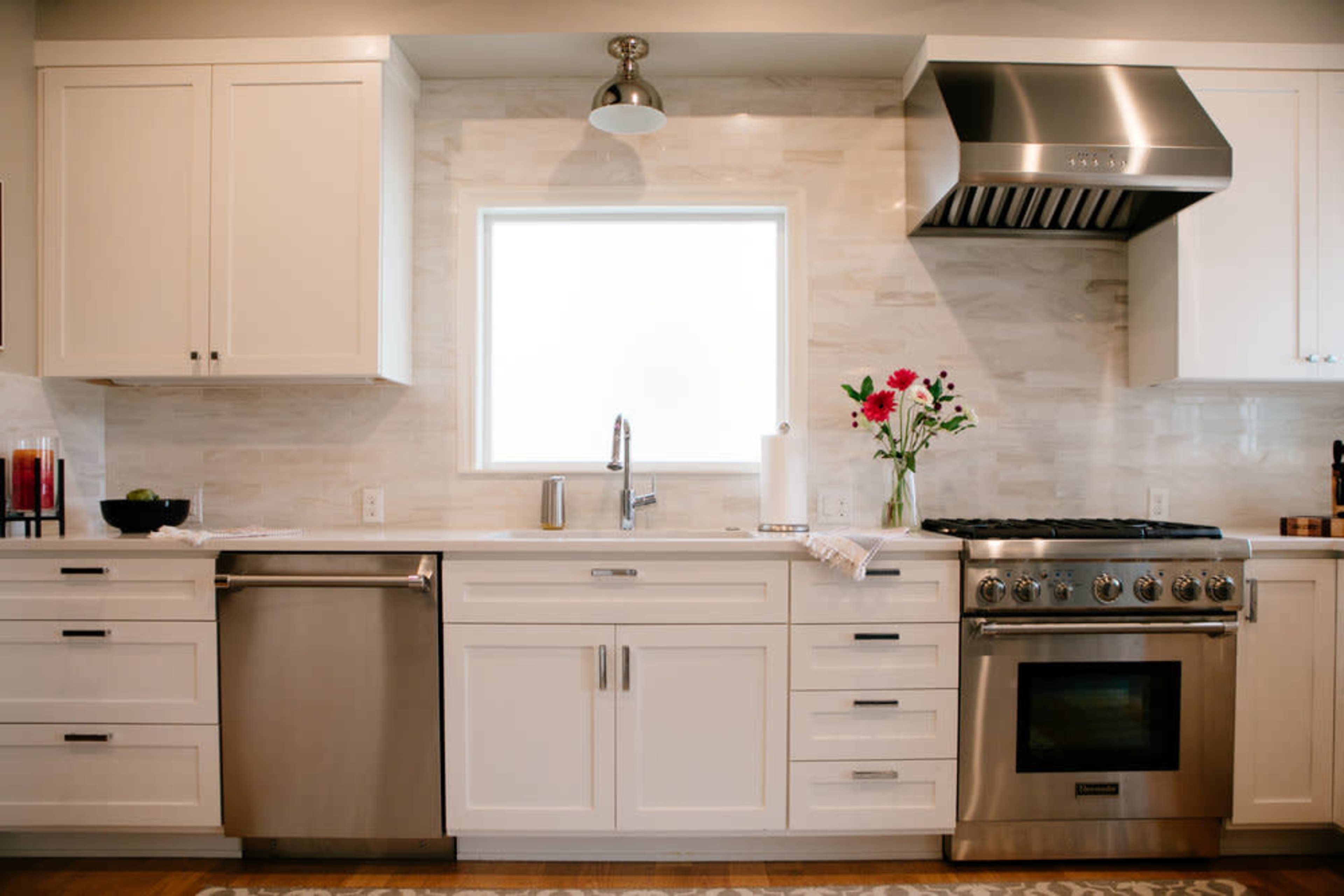 A modern kitchen with white cabinets, a stainless steel refrigerator and oven, and a window above the sink.