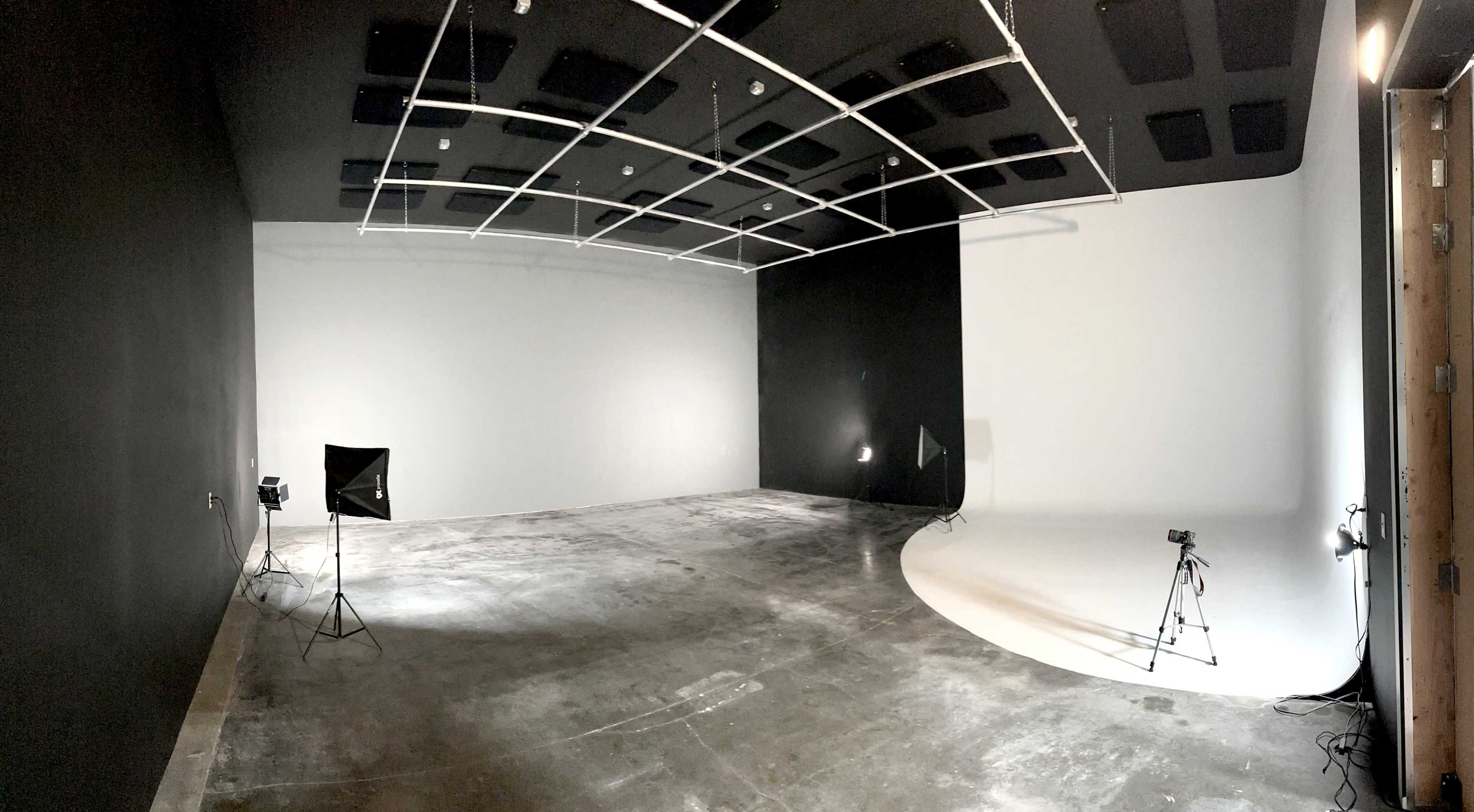 A spacious photography studio with a black wall on one side and a white backdrop on the other, along with lighting equipment and tripods set up.