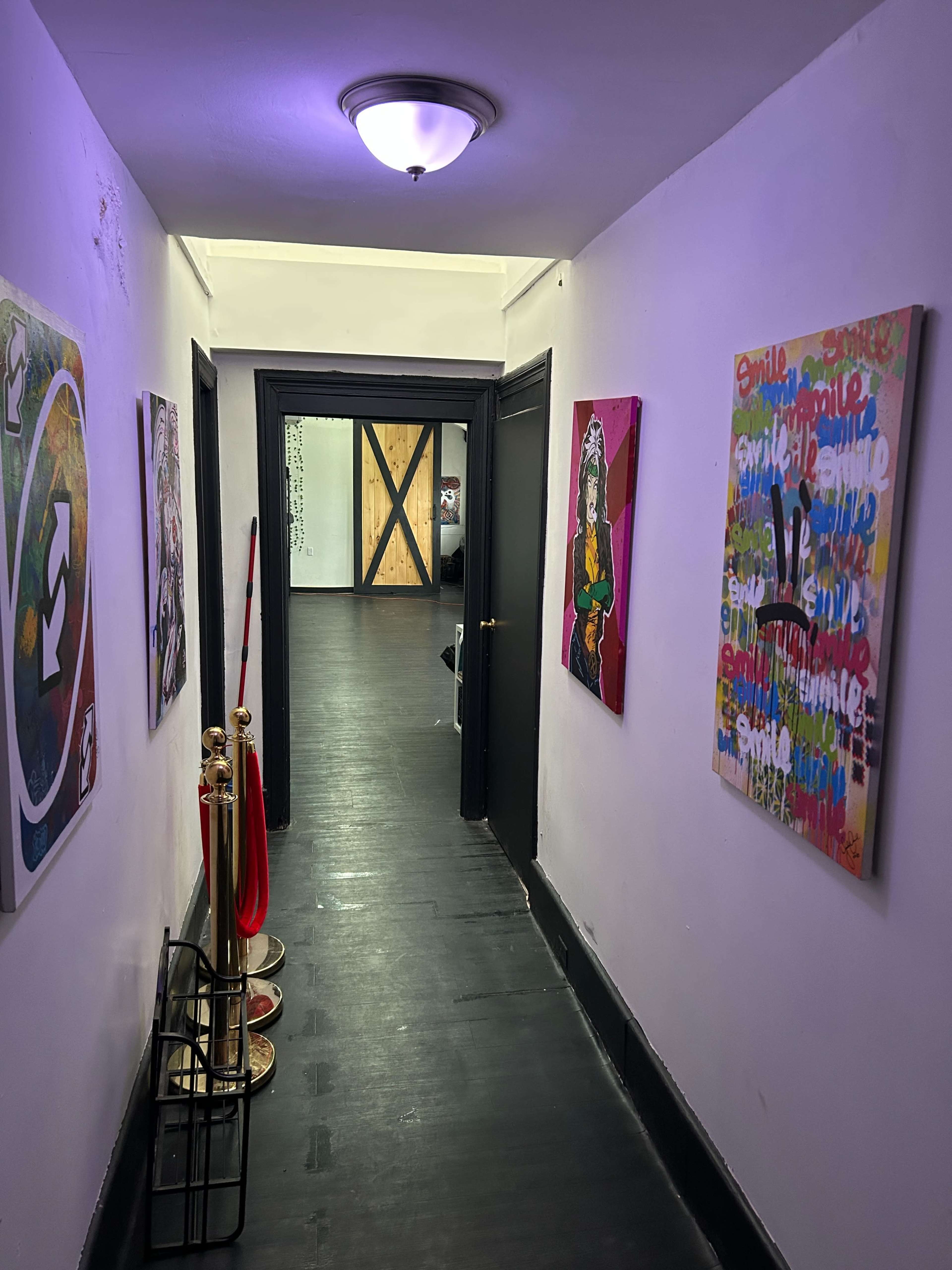 The image shows a narrow hallway with colorful artwork on the walls, leading to a door at the end.
