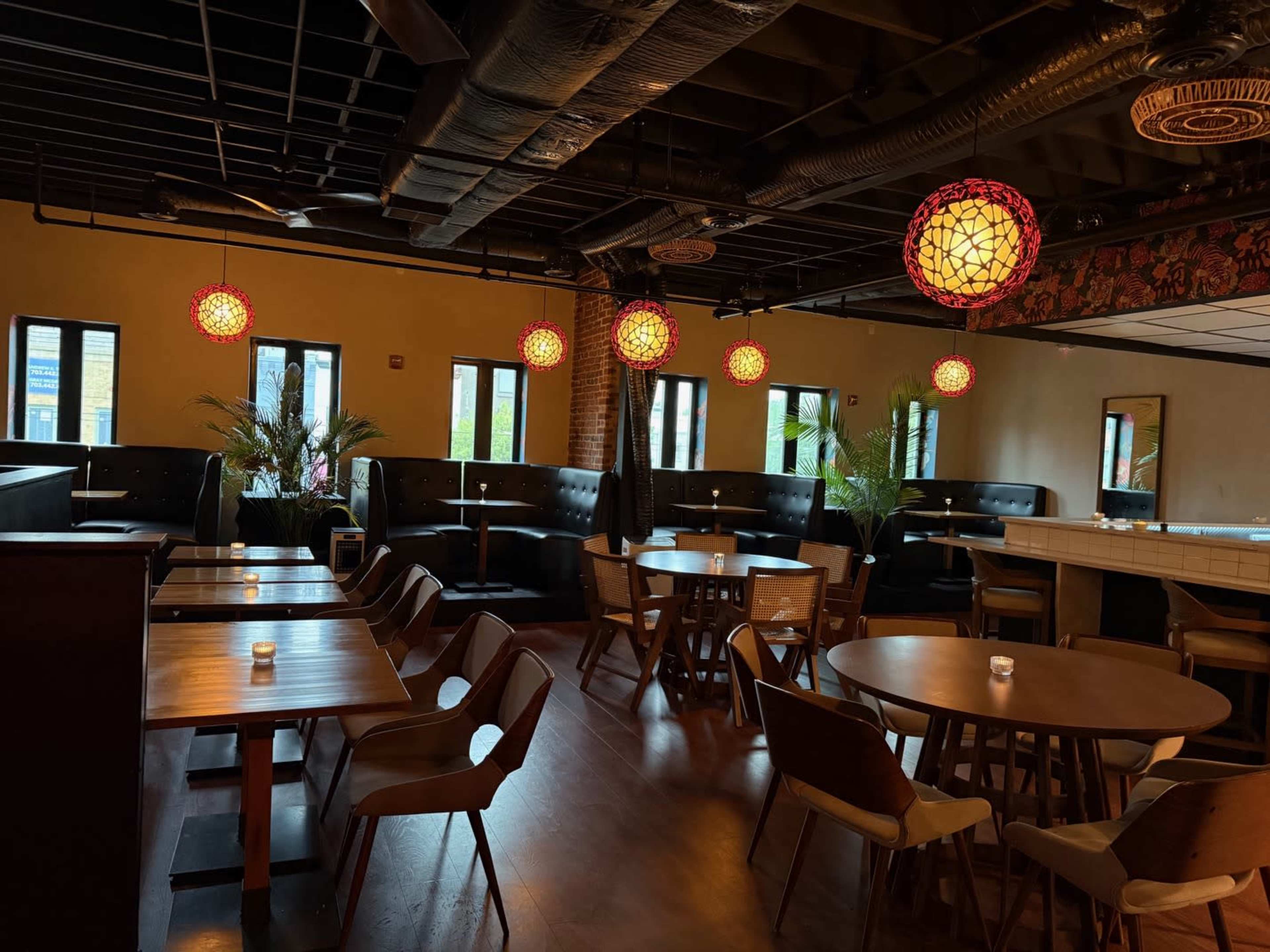 The image shows a modern restaurant interior with wooden tables, chairs, and decorative pendant lights hanging from the ceiling.