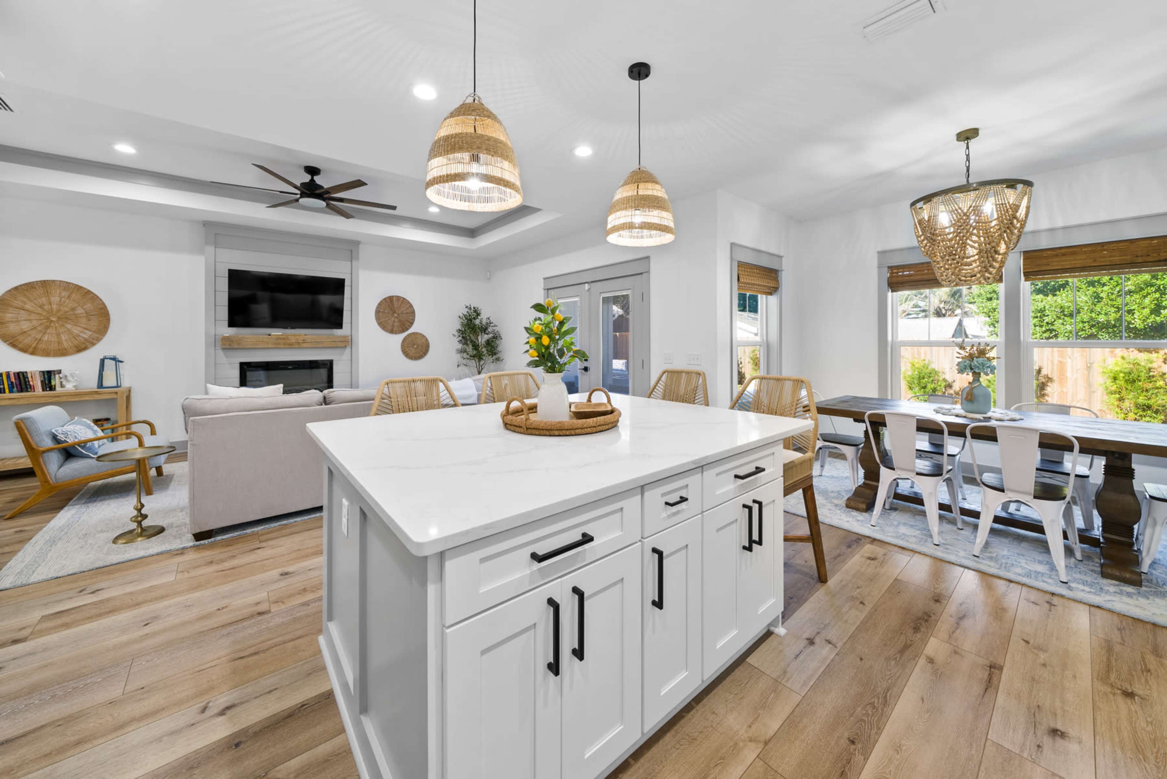 A modern kitchen and dining area feature an island with seating, a dining table, and large windows overlooking a backyard.