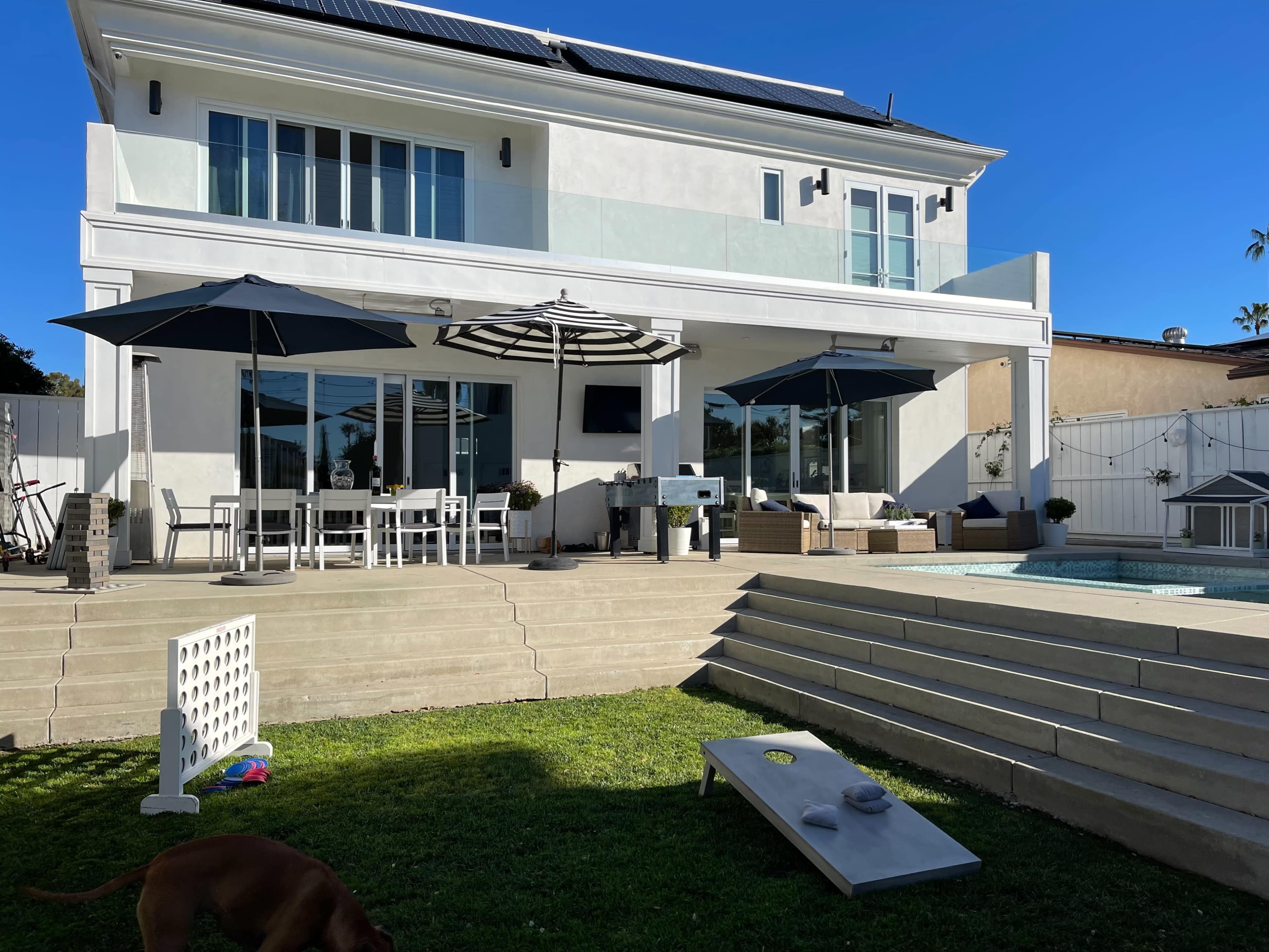A modern two-story house with a backyard featuring a swimming pool, outdoor seating area, and patio umbrellas.