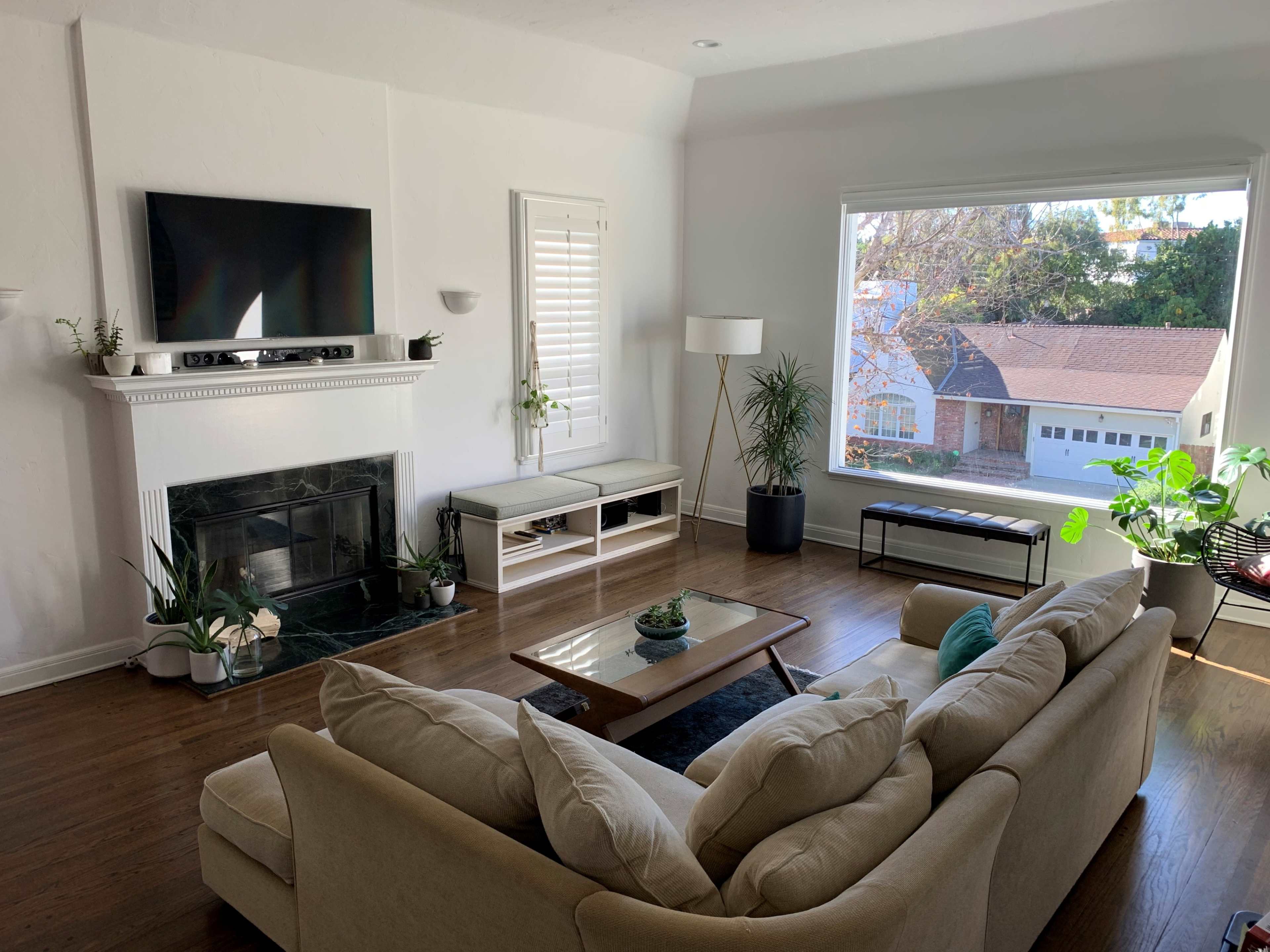 A bright living room features a beige sofa, a coffee table, and a large window showcasing outdoor greenery.