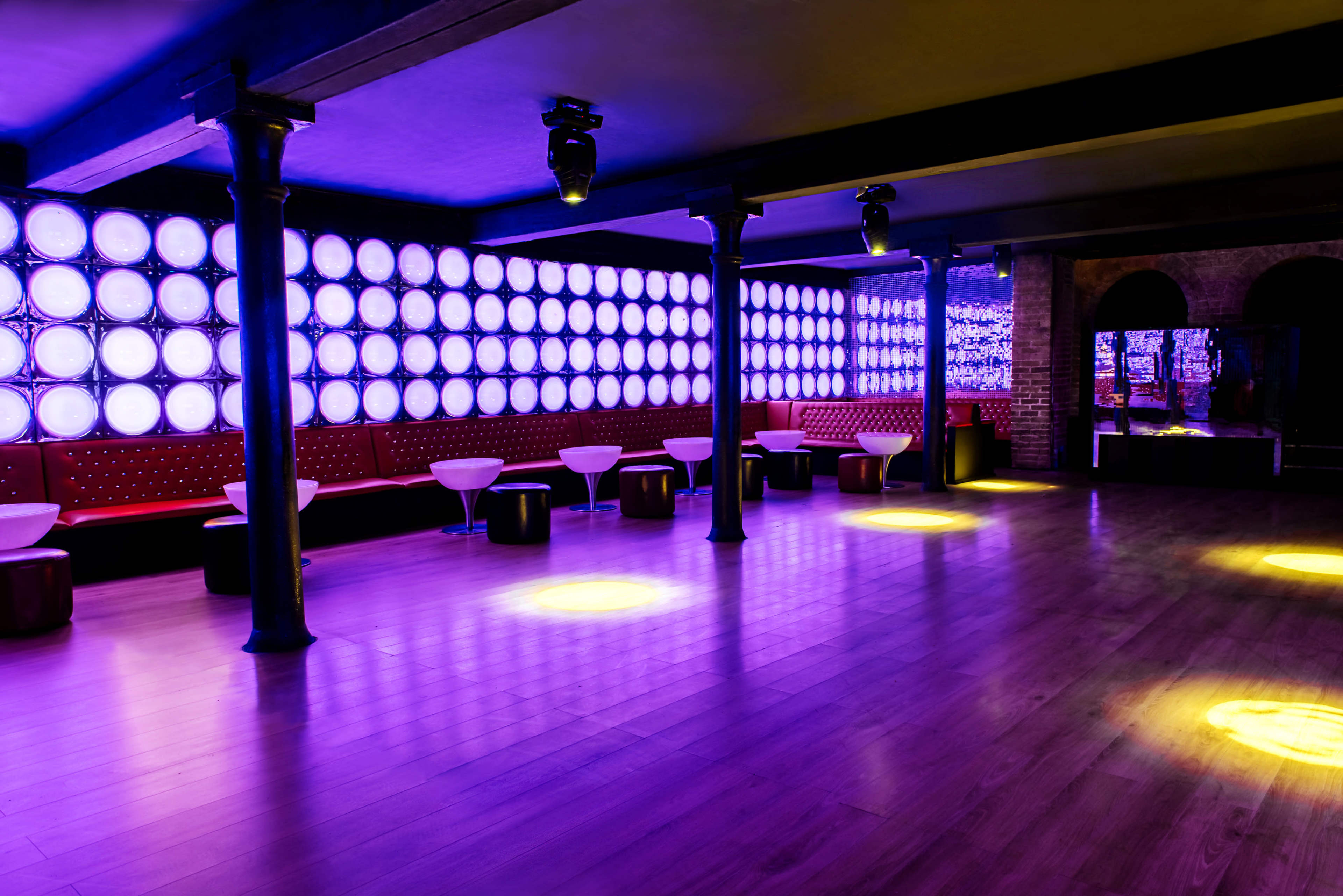 A spacious nightclub interior features illuminated walls and circular seating arrangements under soft lighting.