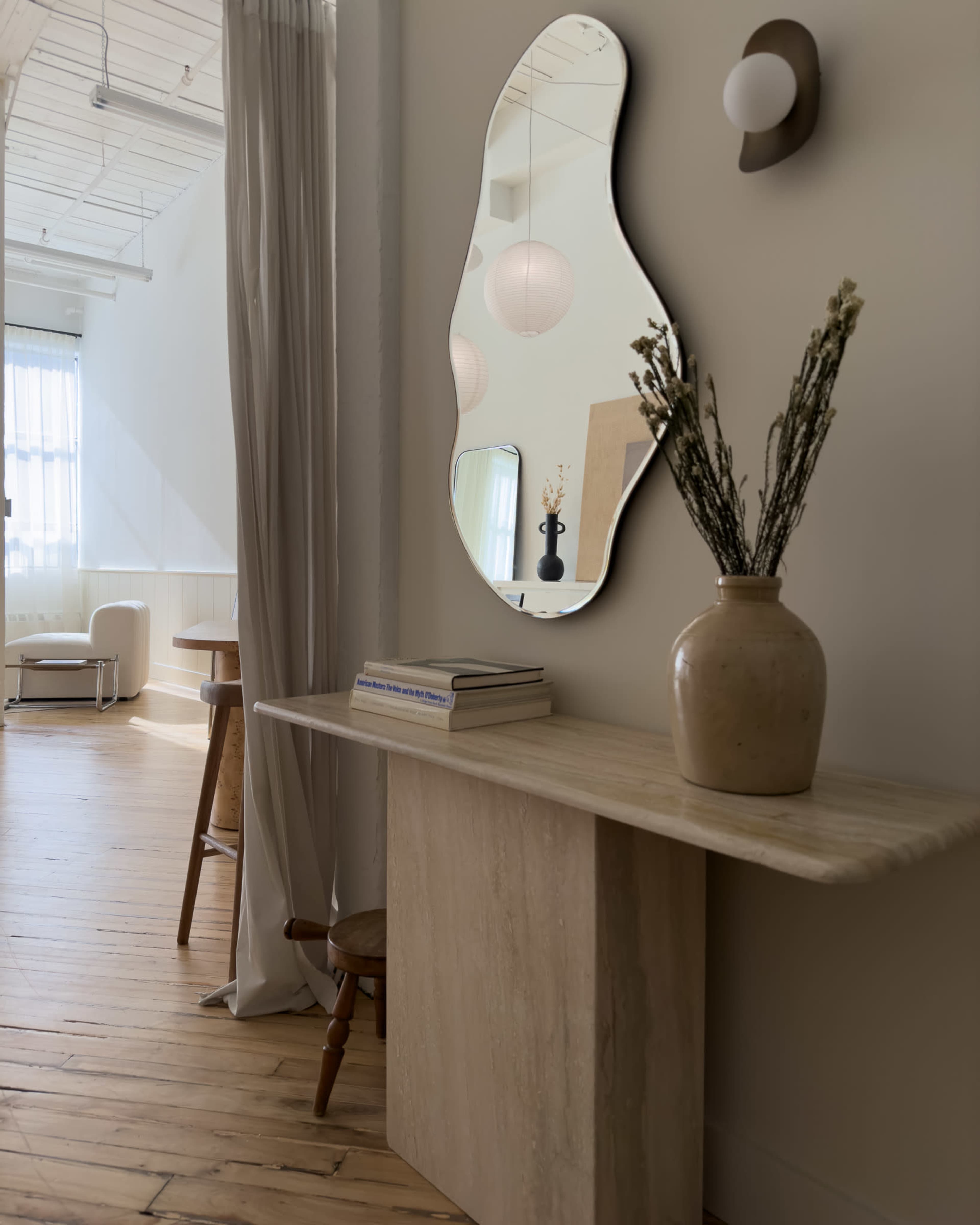 A minimalist entryway features a stone console table with a stylish mirror above it, a decorative vase, and soft lighting.