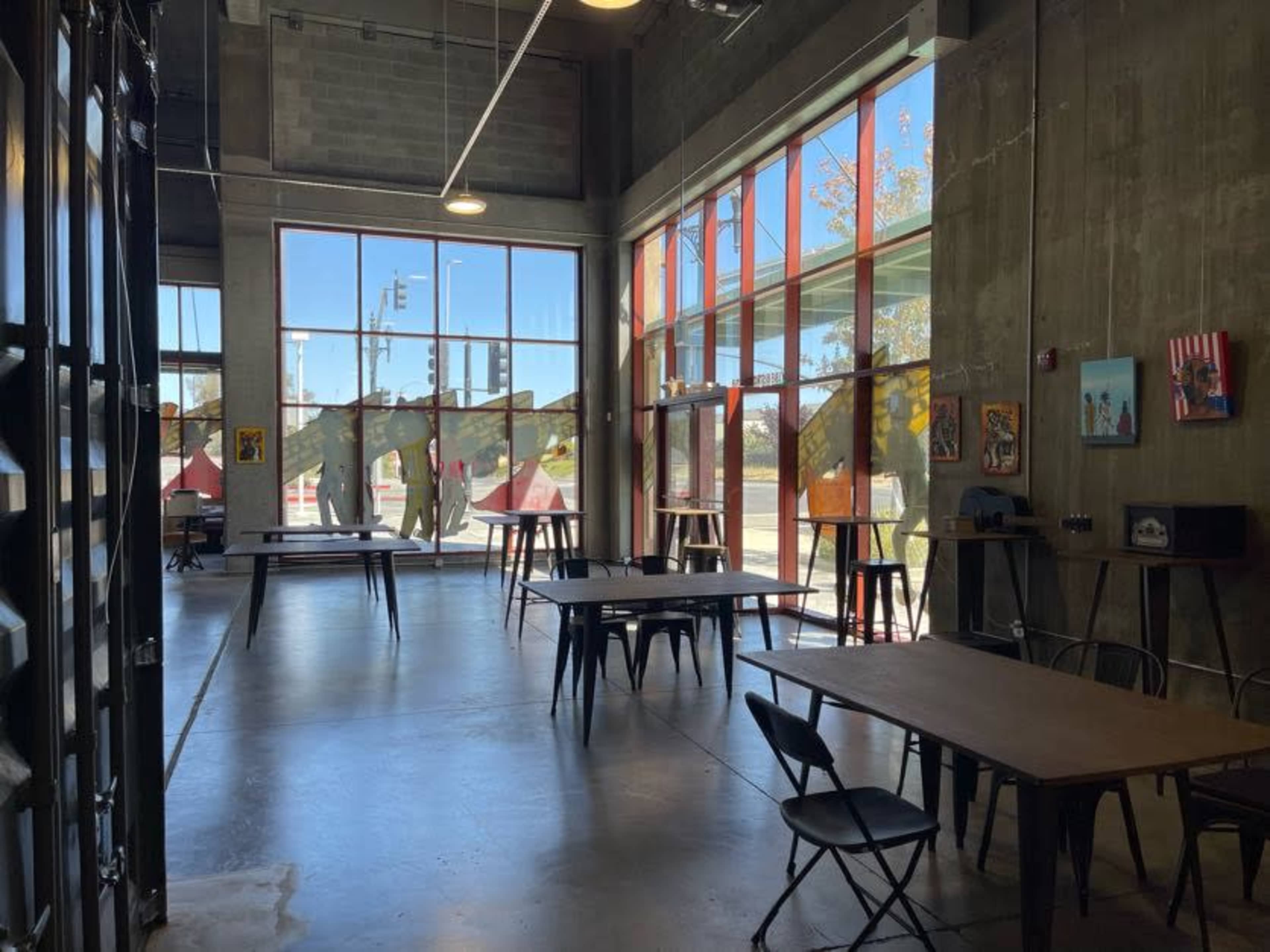 A spacious room with large windows, concrete walls, and several tables and chairs arranged for use.