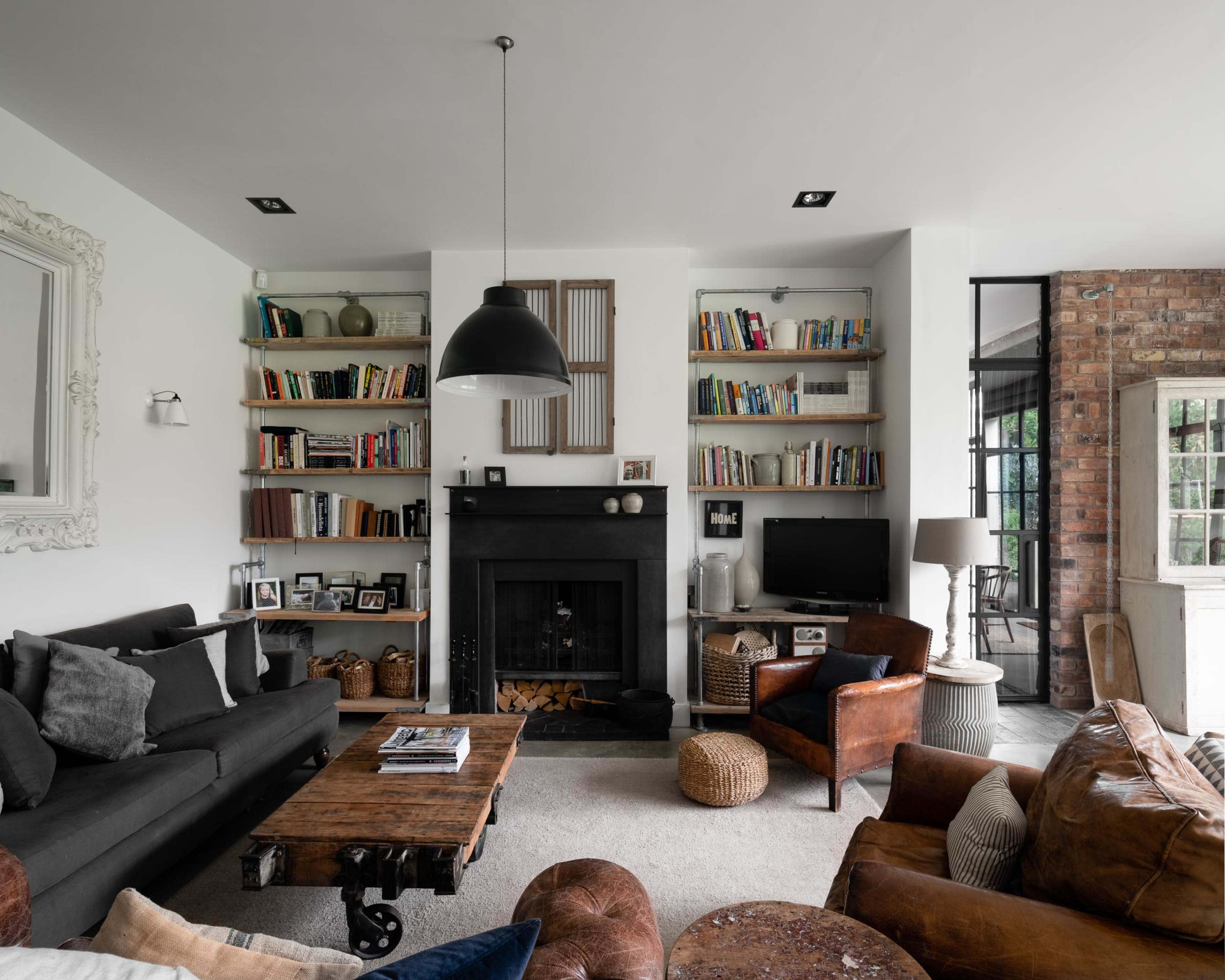 A modern living room with a dark fireplace, bookshelves filled with books, and a mix of comfortable seating arrangements.