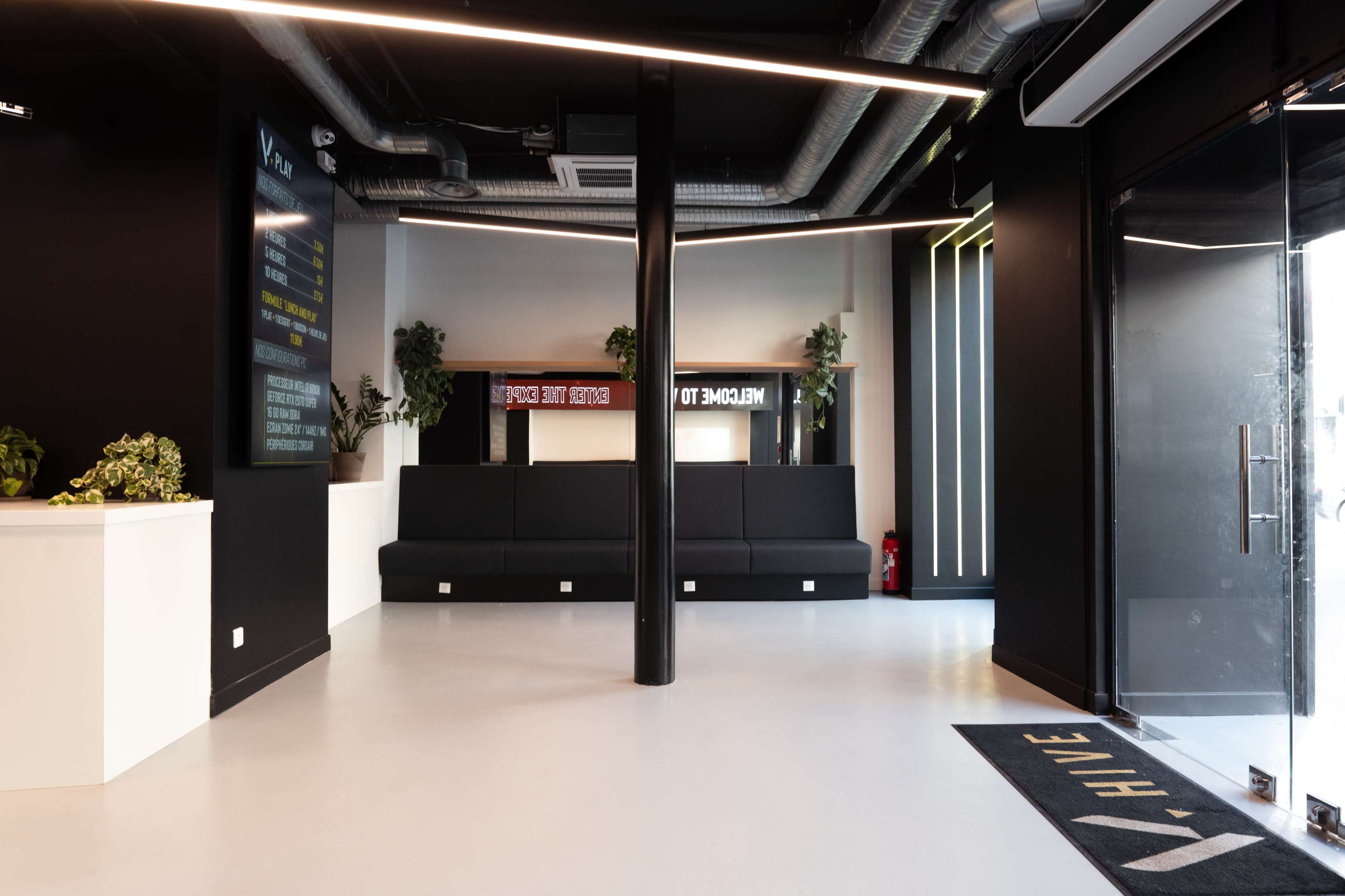 The image shows a modern reception area with black walls, a large seating area, and a glass entrance door.
