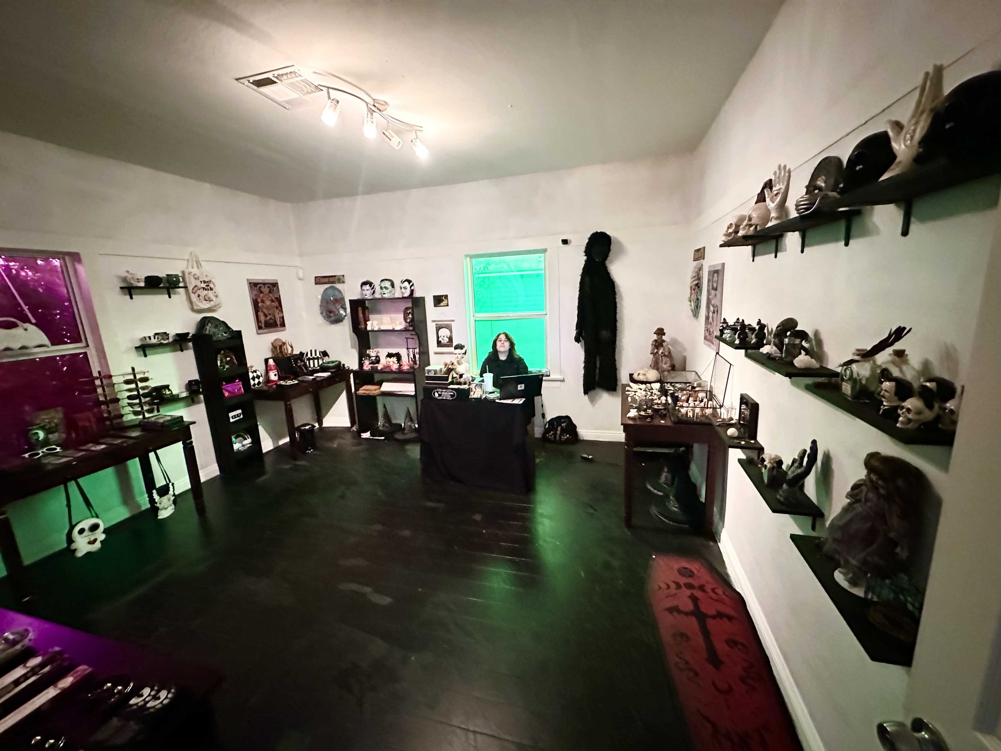 A person sits at a desk in a dimly lit room filled with various decorative items and shelves displaying a collection of masks and sculptures.