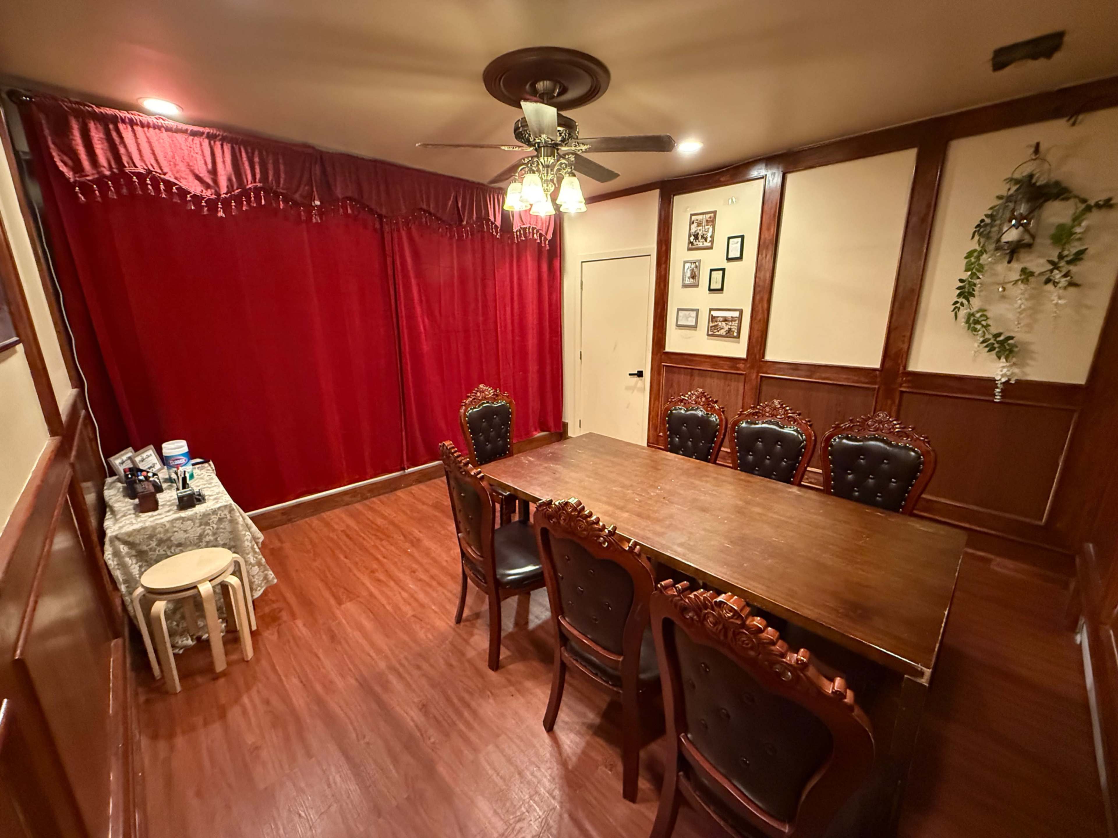 The image shows a dining room with a wooden table surrounded by eight ornate chairs, and a red curtain covering one wall.