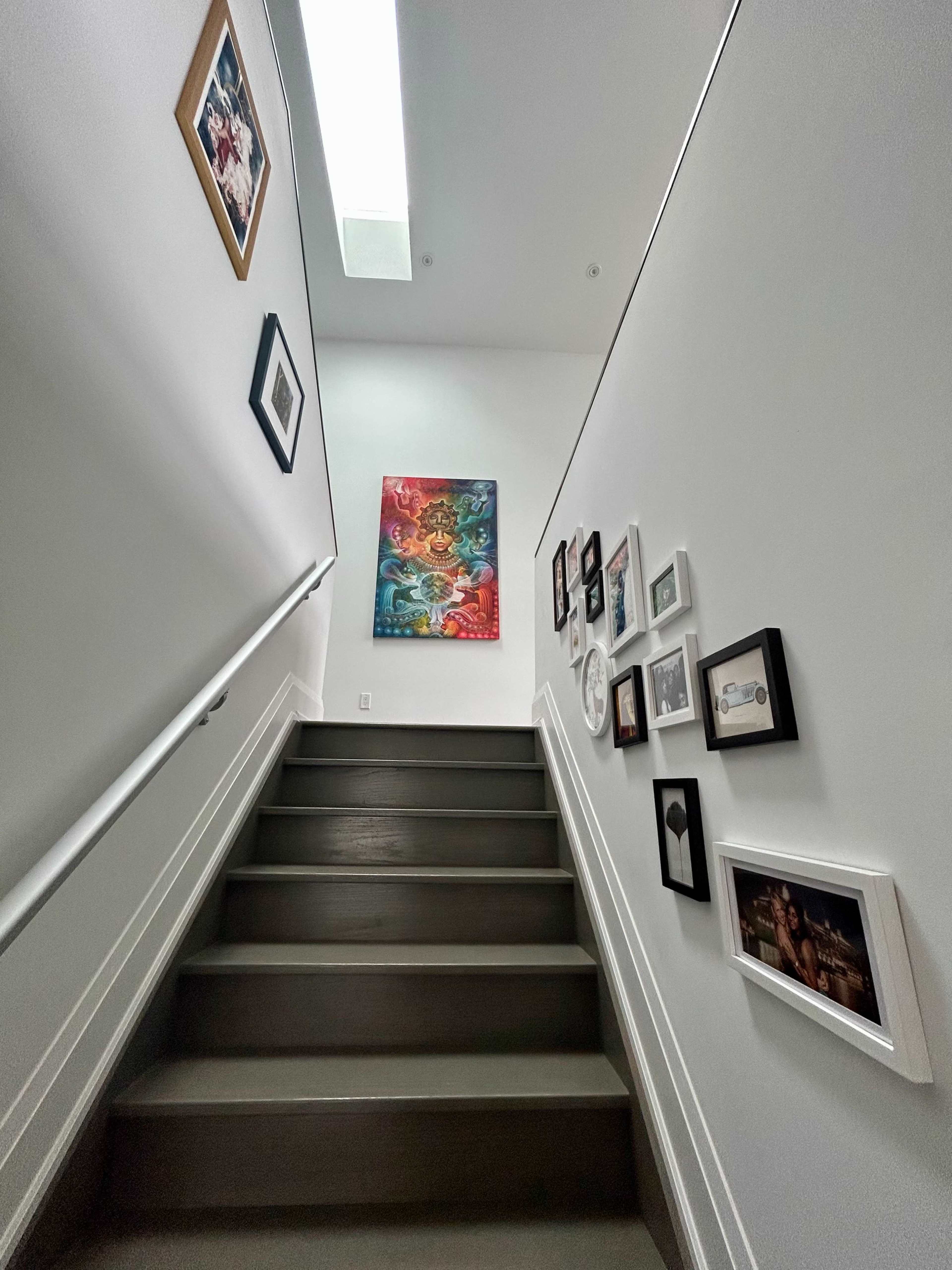 A staircase leads upward, flanked by pictures framed on the wall and a large painting at the top.