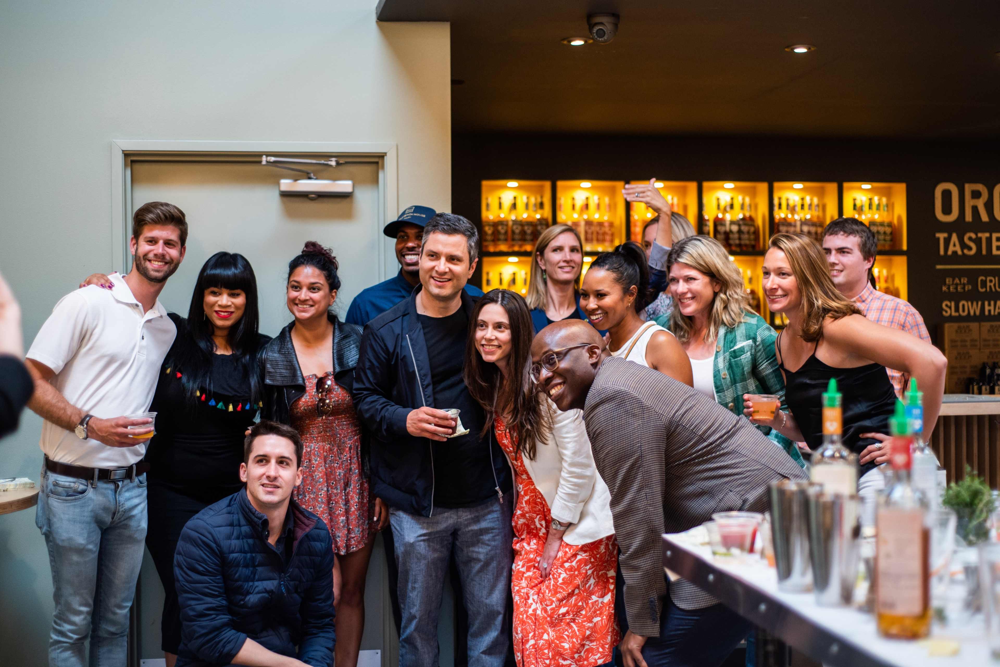 A group of people poses for a photo in a social setting with a bar in the background.