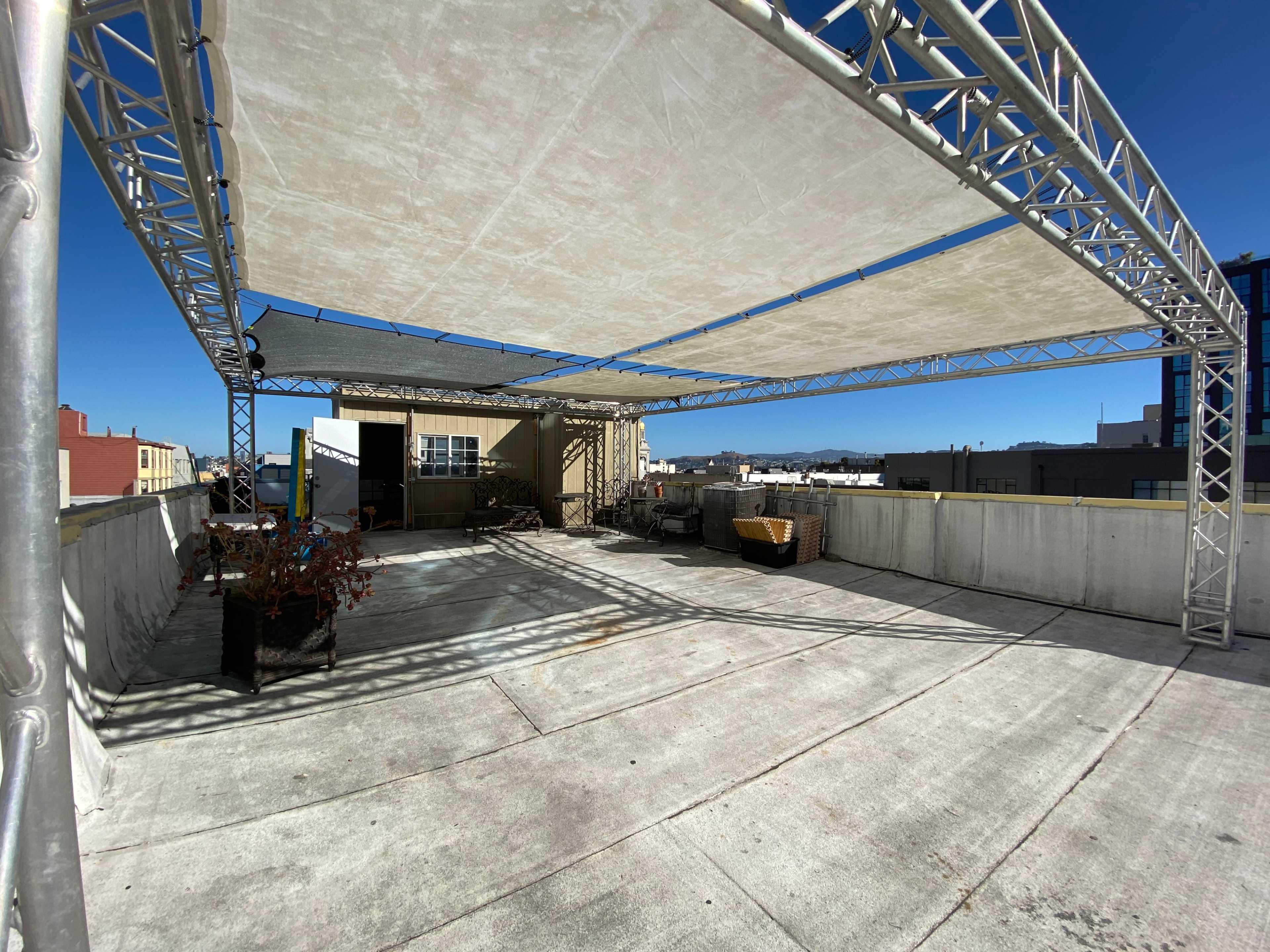 A rooftop space is covered by a large fabric canopy, with various items and planters scattered around.