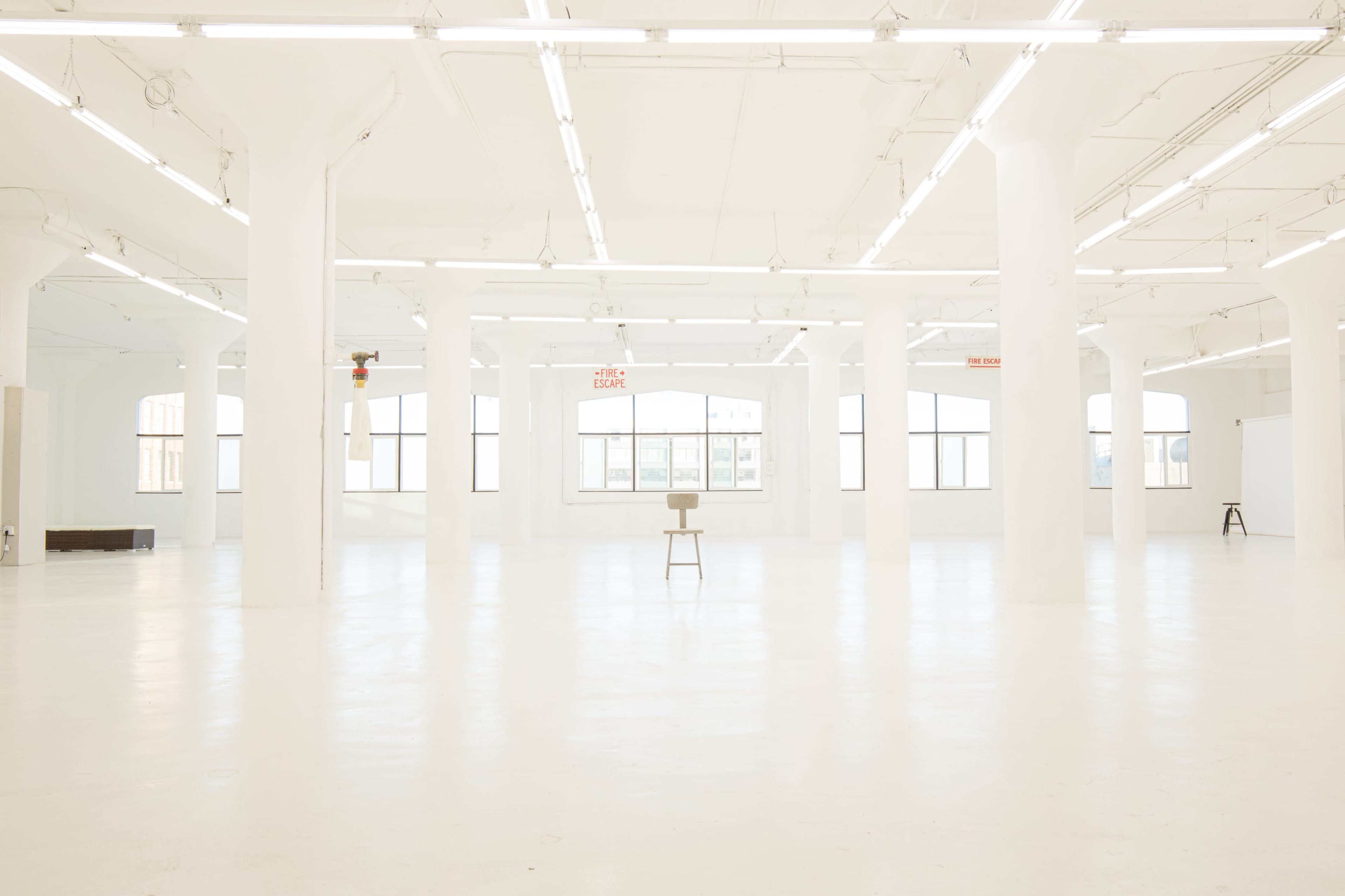 A spacious, well-lit white room with tall pillars and a single stool in the center.