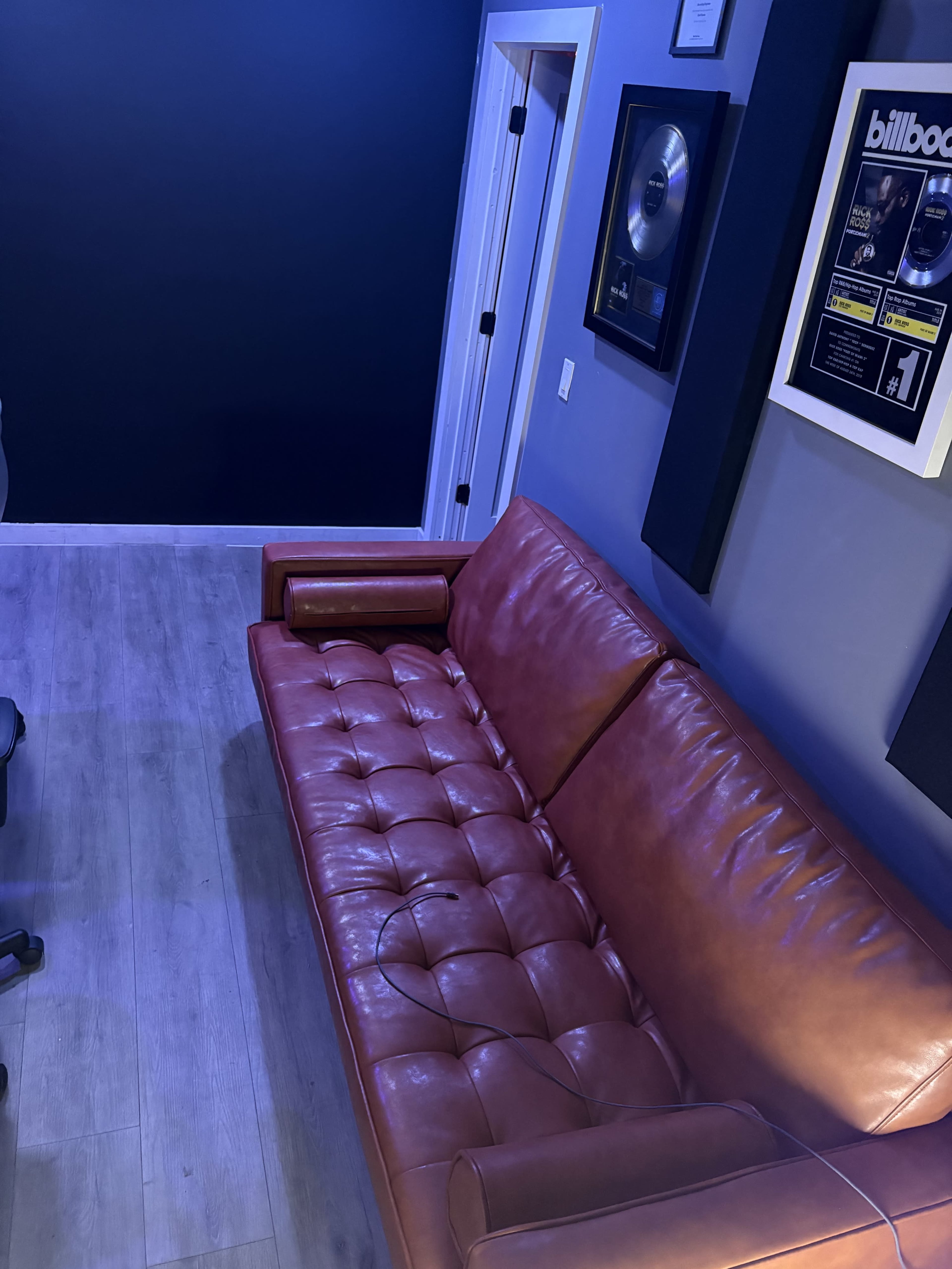 The image shows a leather couch positioned against a wall with framed awards and soundproofing panels nearby.