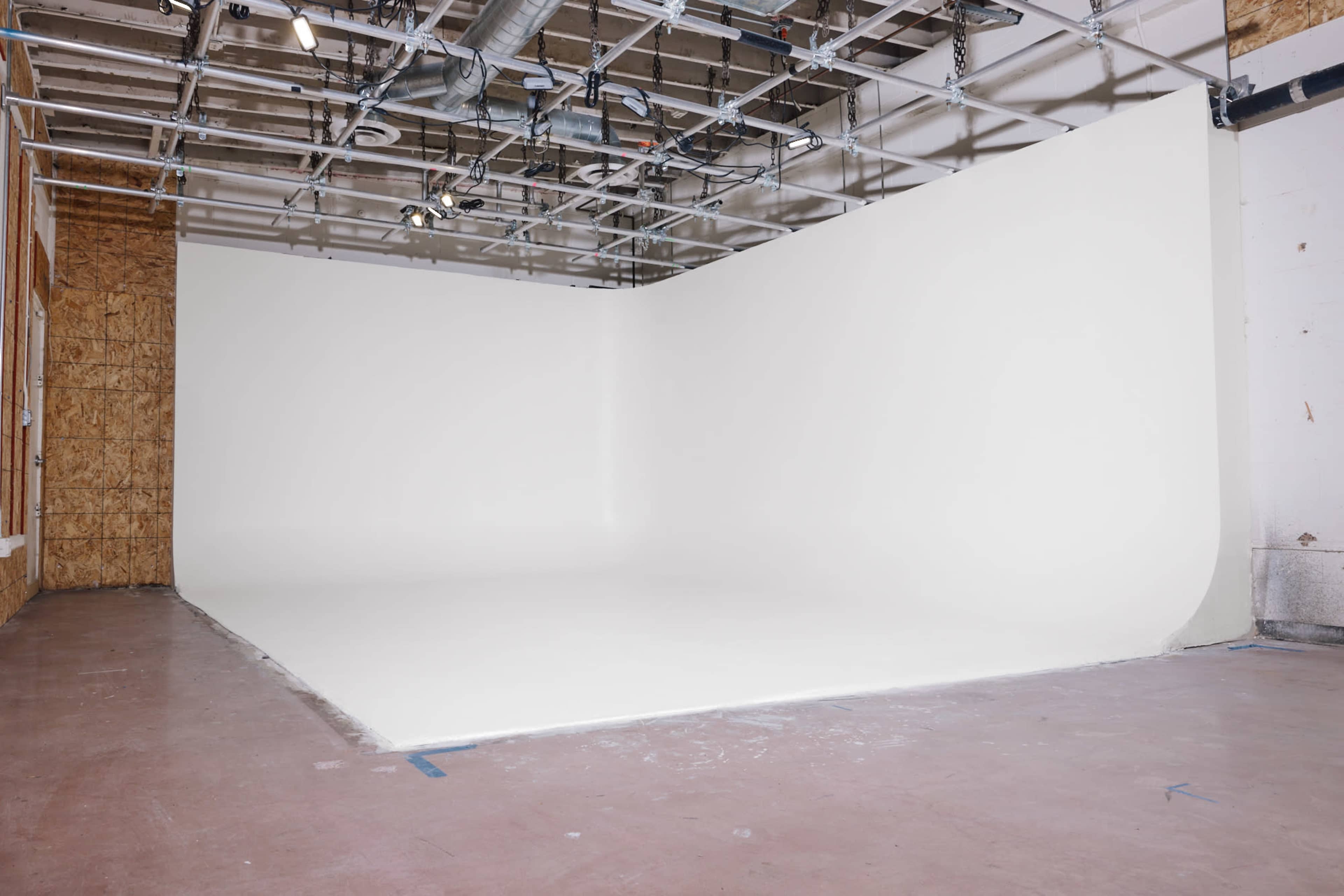 The image shows an empty studio space with a seamless white backdrop and exposed ceiling beams.