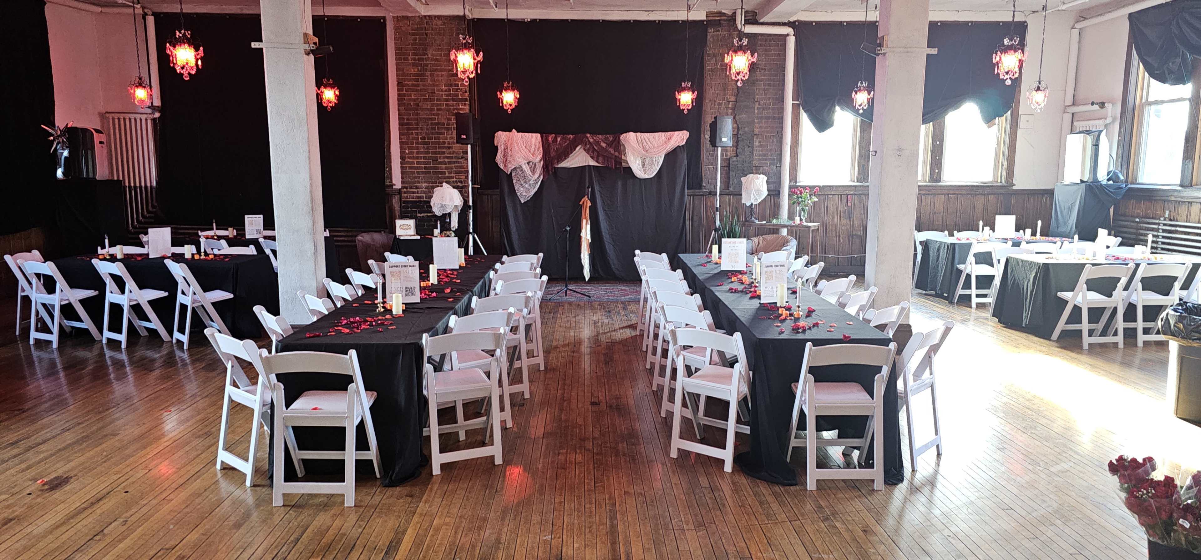 The image shows a decorated event space with rows of white chairs arranged around black-covered tables, set up for a gathering with red decorative accents.