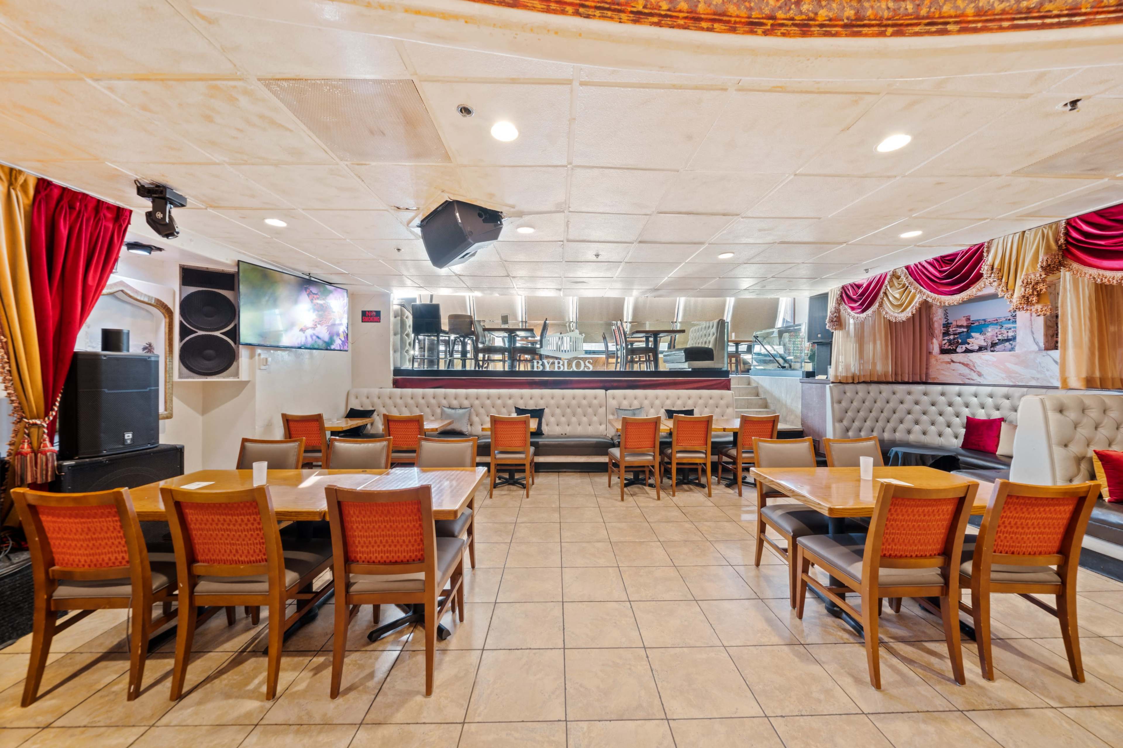 An interior view of a restaurant, featuring several tables and chairs arranged in a spacious layout, with a stage and sound equipment visible at the back.