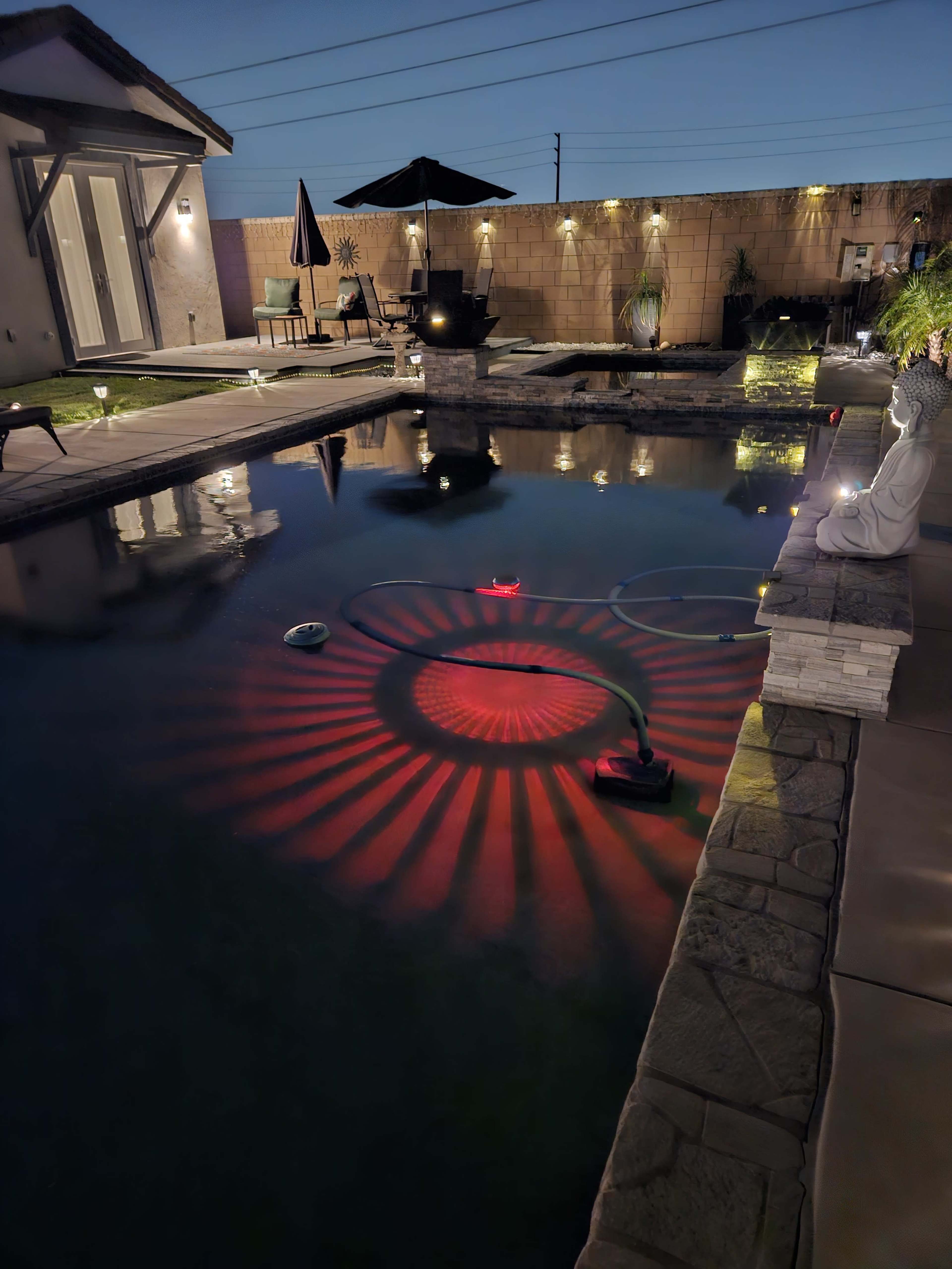 The image shows a backyard pool illuminated by a red light pattern on the water's surface, with furniture and decorations visible around the pool area at dusk.