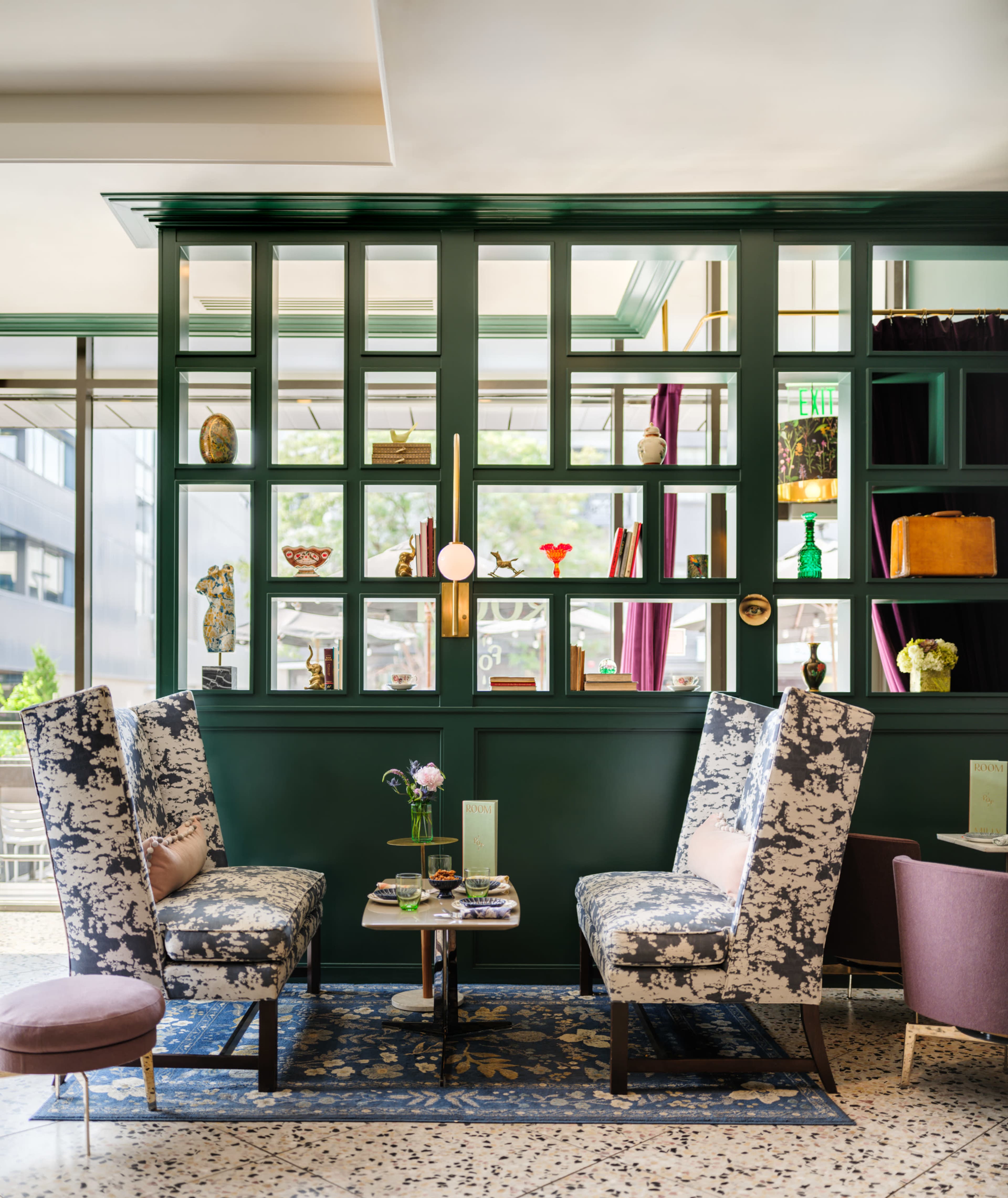 The image shows a stylish café interior with green walls, patterned chairs, and decorative shelves displaying various items.
