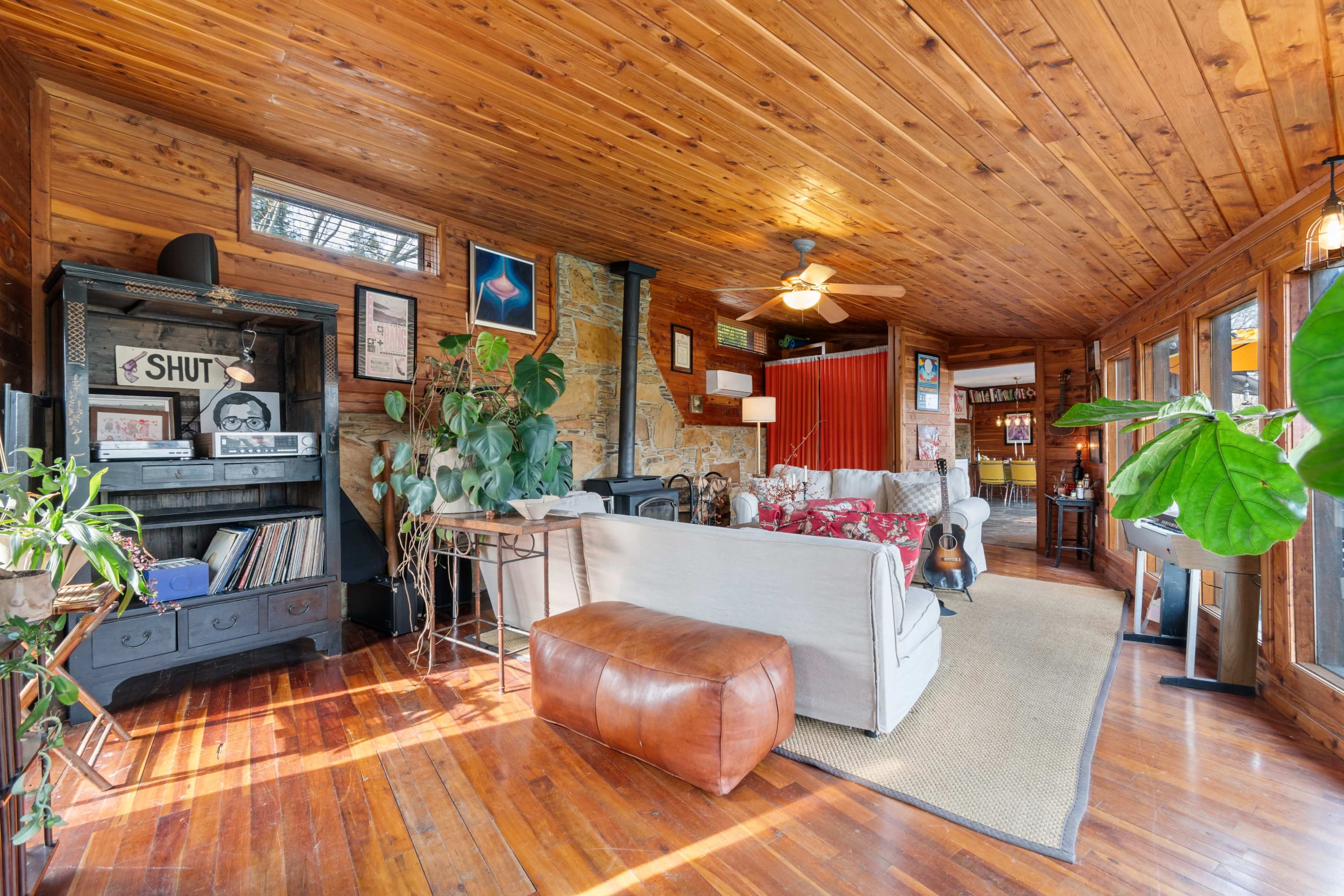 The room features wooden walls and ceiling, a mix of furniture, plants, and a seating area with a sofa and a coffee table.