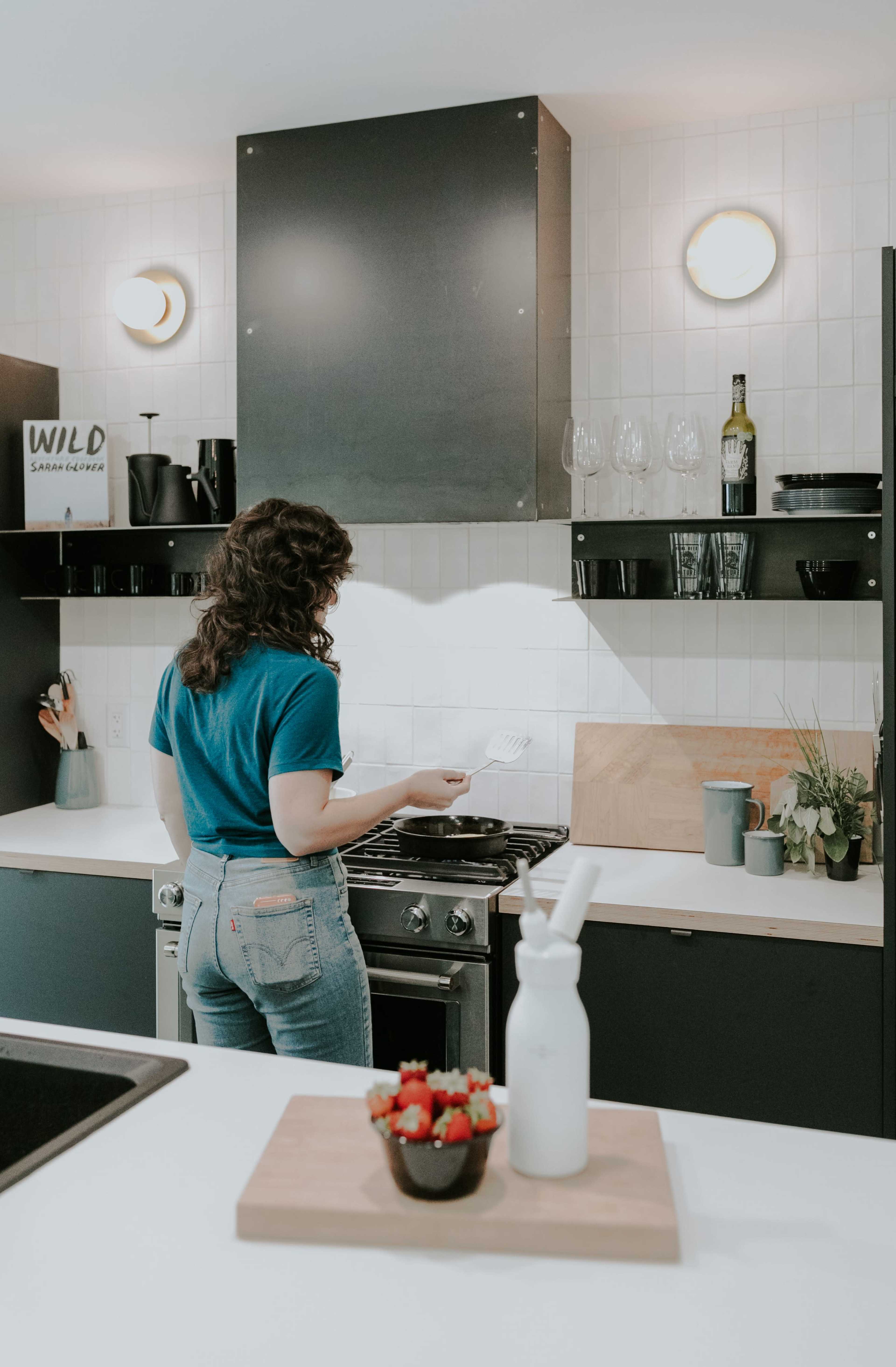 A person with curly hair stands at a stove in a modern kitchen, preparing food.