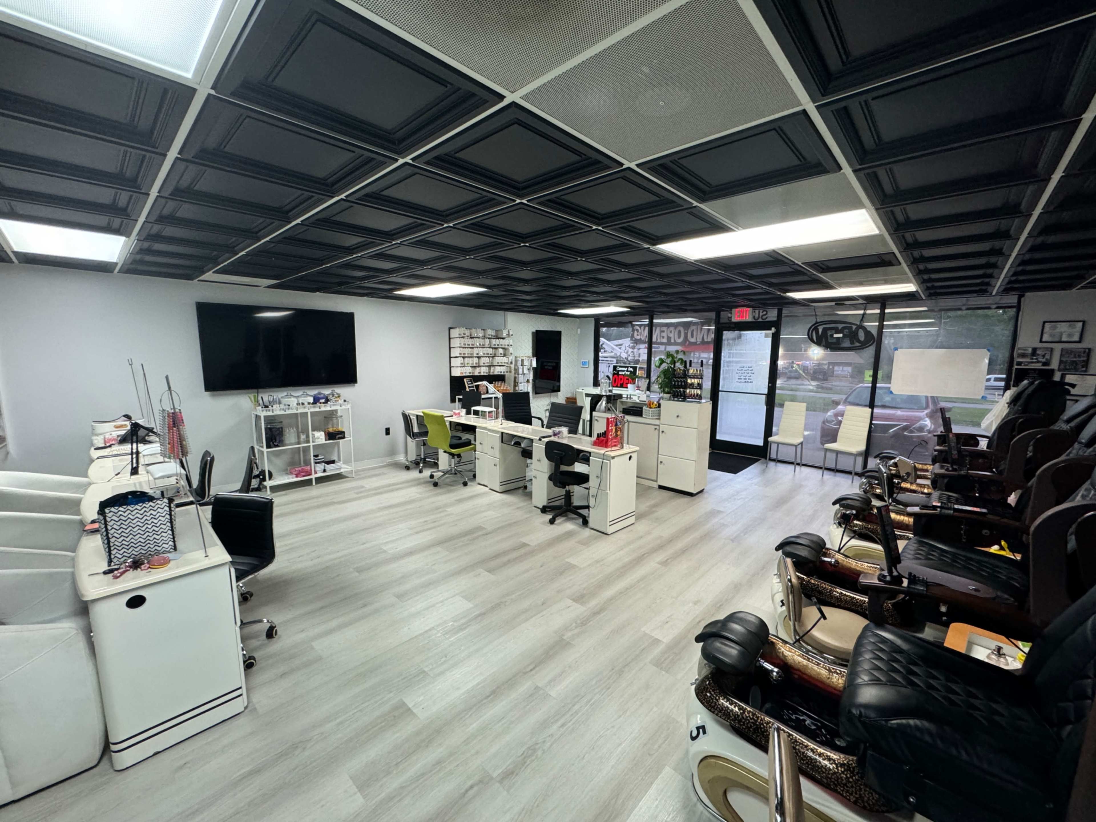 The image shows a nail salon interior featuring manicure stations on one side and pedicure chairs on the other, with a reception area in the center.