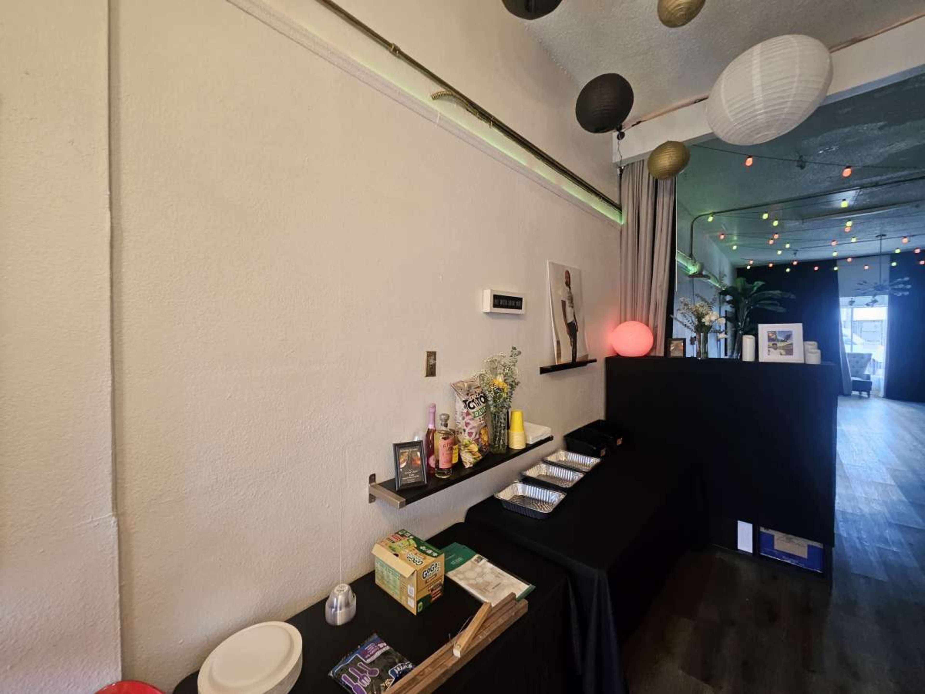 A table covered with a black cloth displays snacks and drinks in a well-lit room decorated with hanging paper lanterns.
