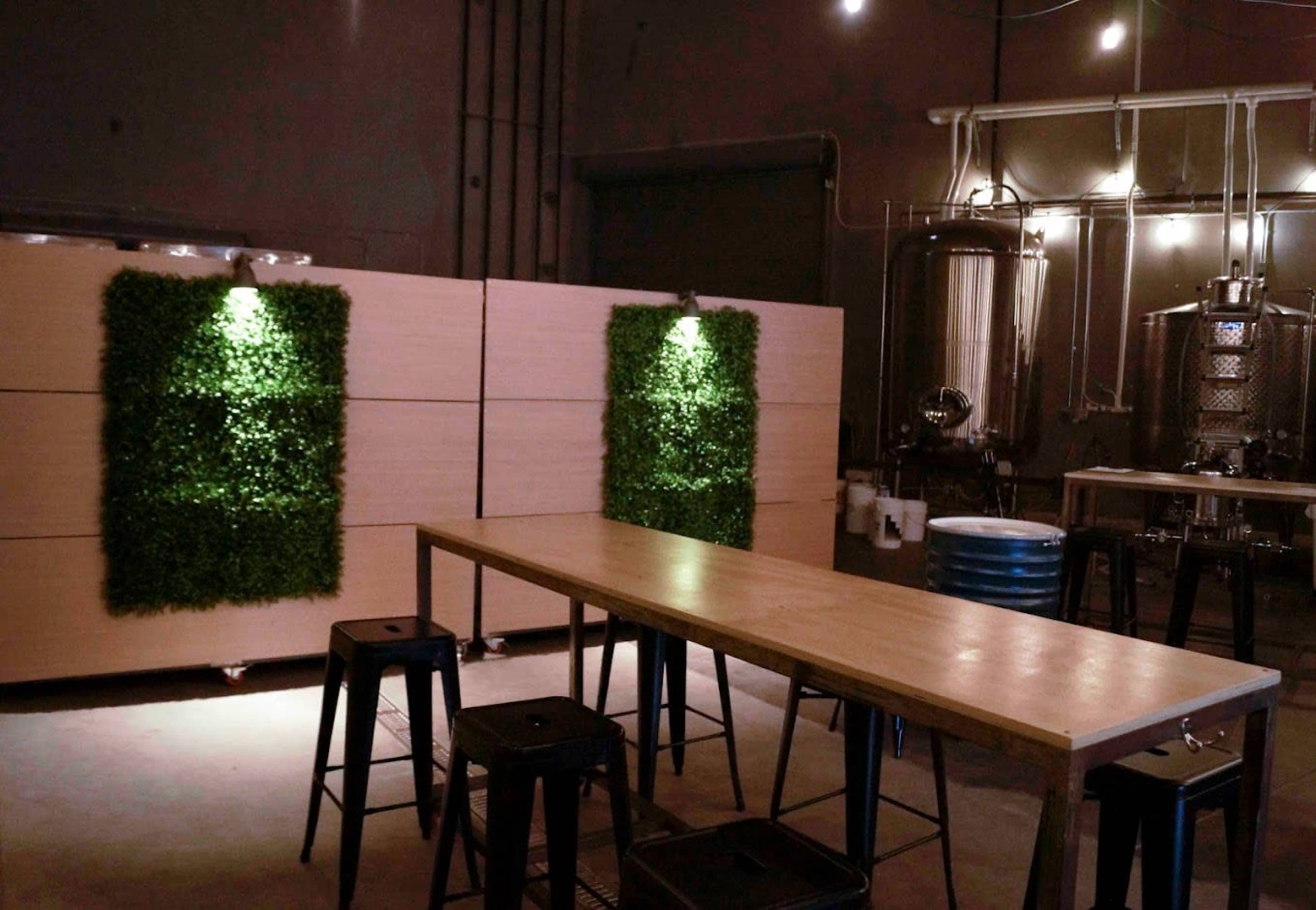 A brewery interior featuring wooden furniture, green wall accents, and brewing equipment in the background.